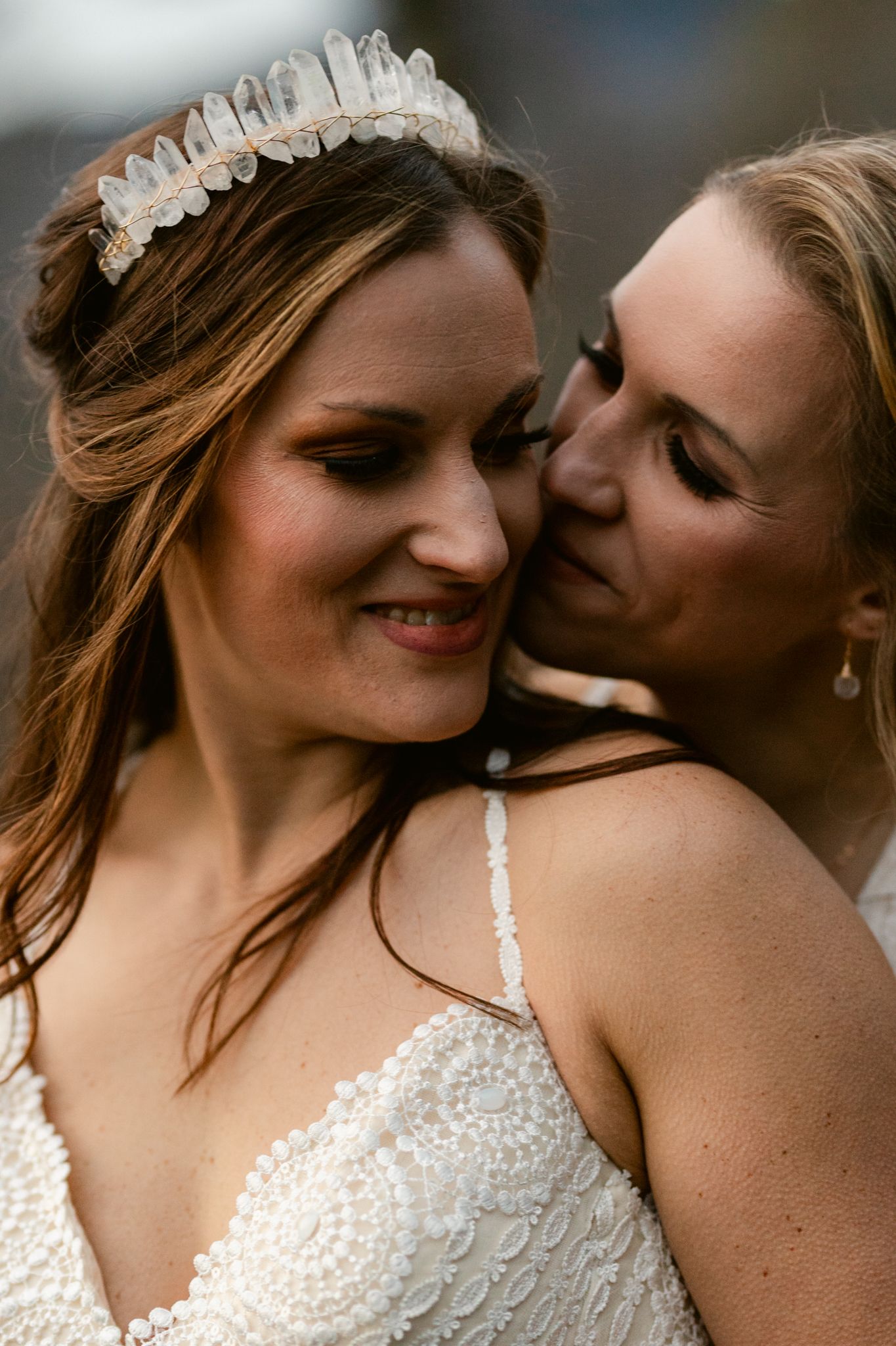 Intimate close-up moment between two people wearing white lace dresses and delicate hair accessories.