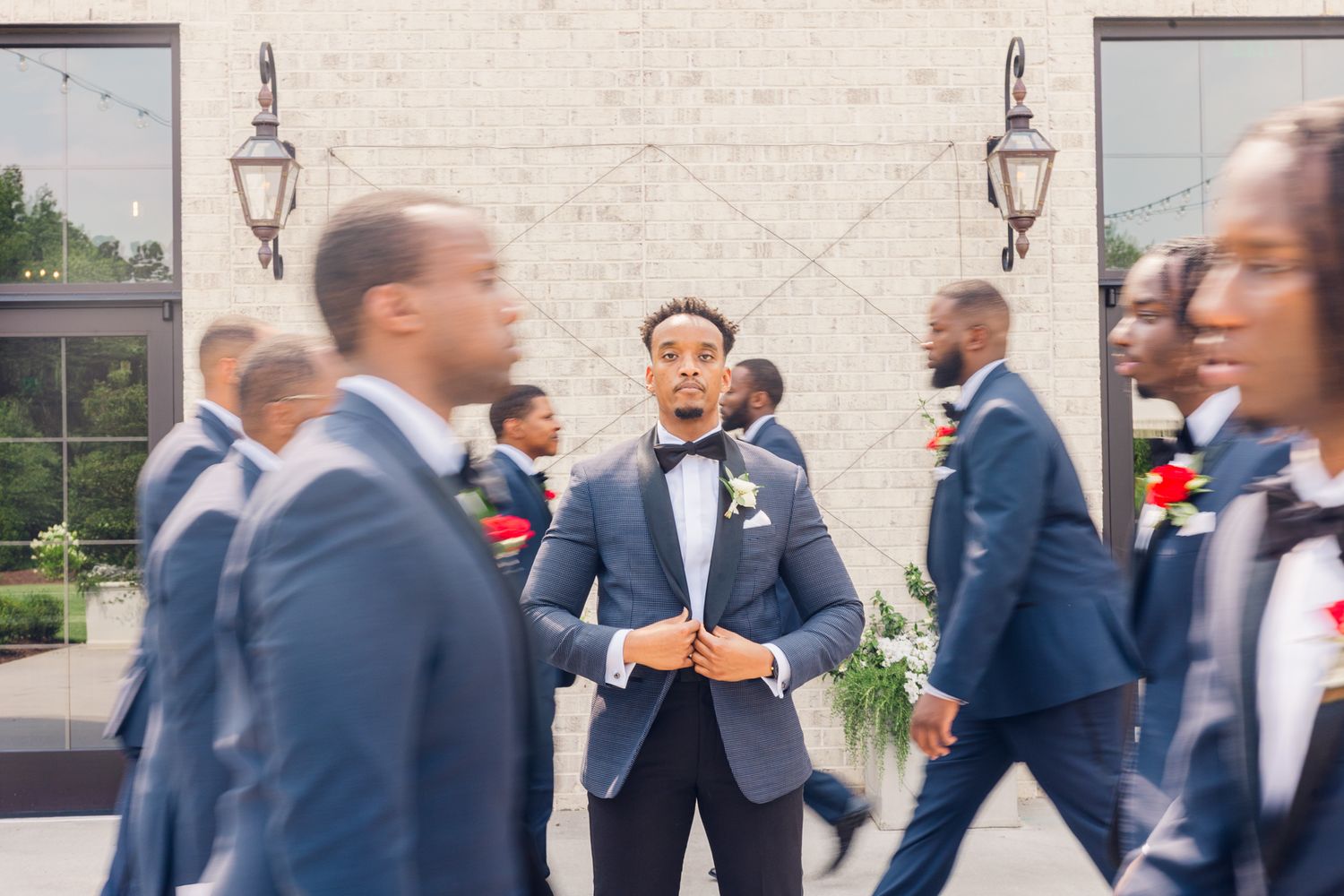 Groomsmen in navy suits share joyful moments and embraces during an outdoor wedding celebration.