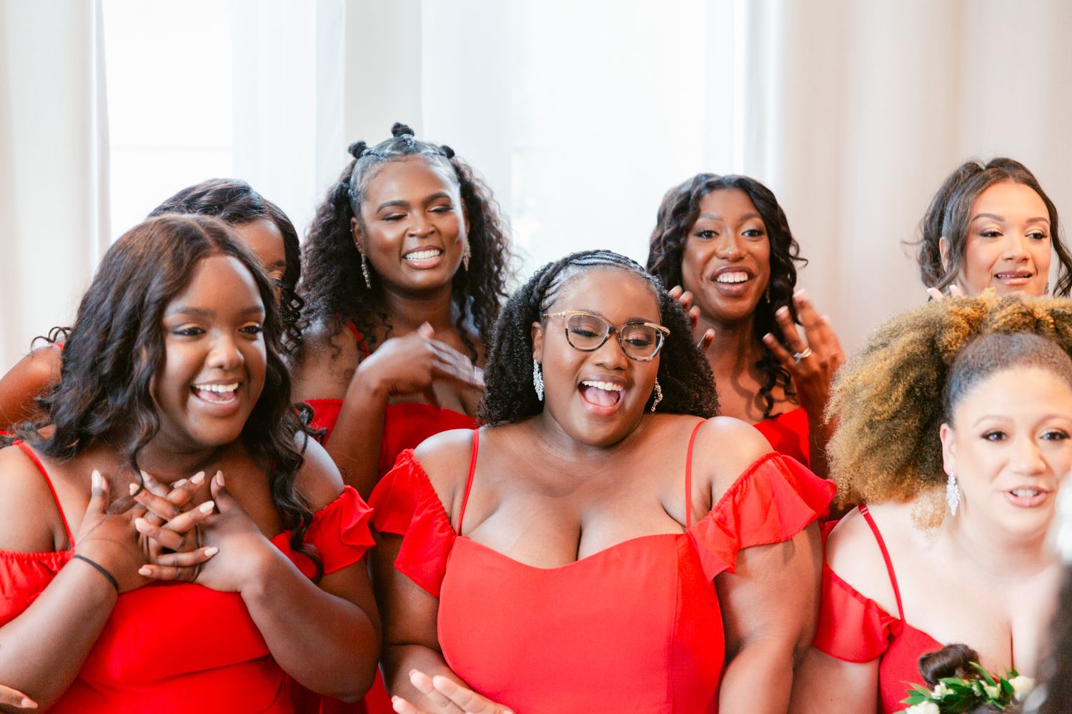 A group of women in red dresses pose together in a joyful group photo.