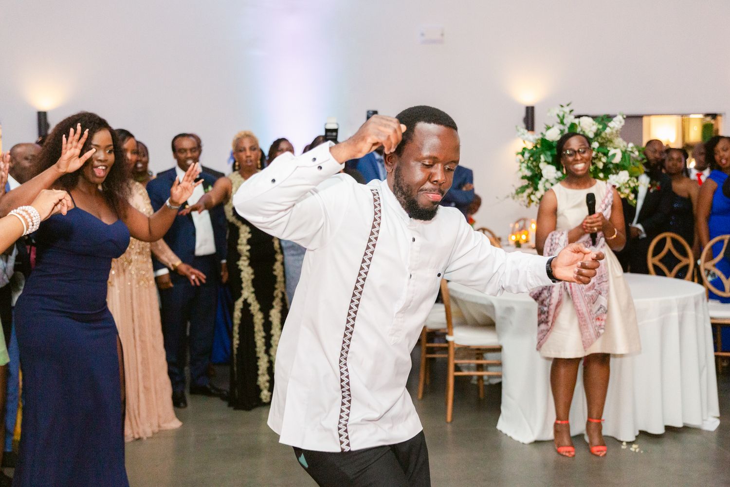 Wedding guests dancing and celebrating on a bright white dance floor at an indoor reception venue.