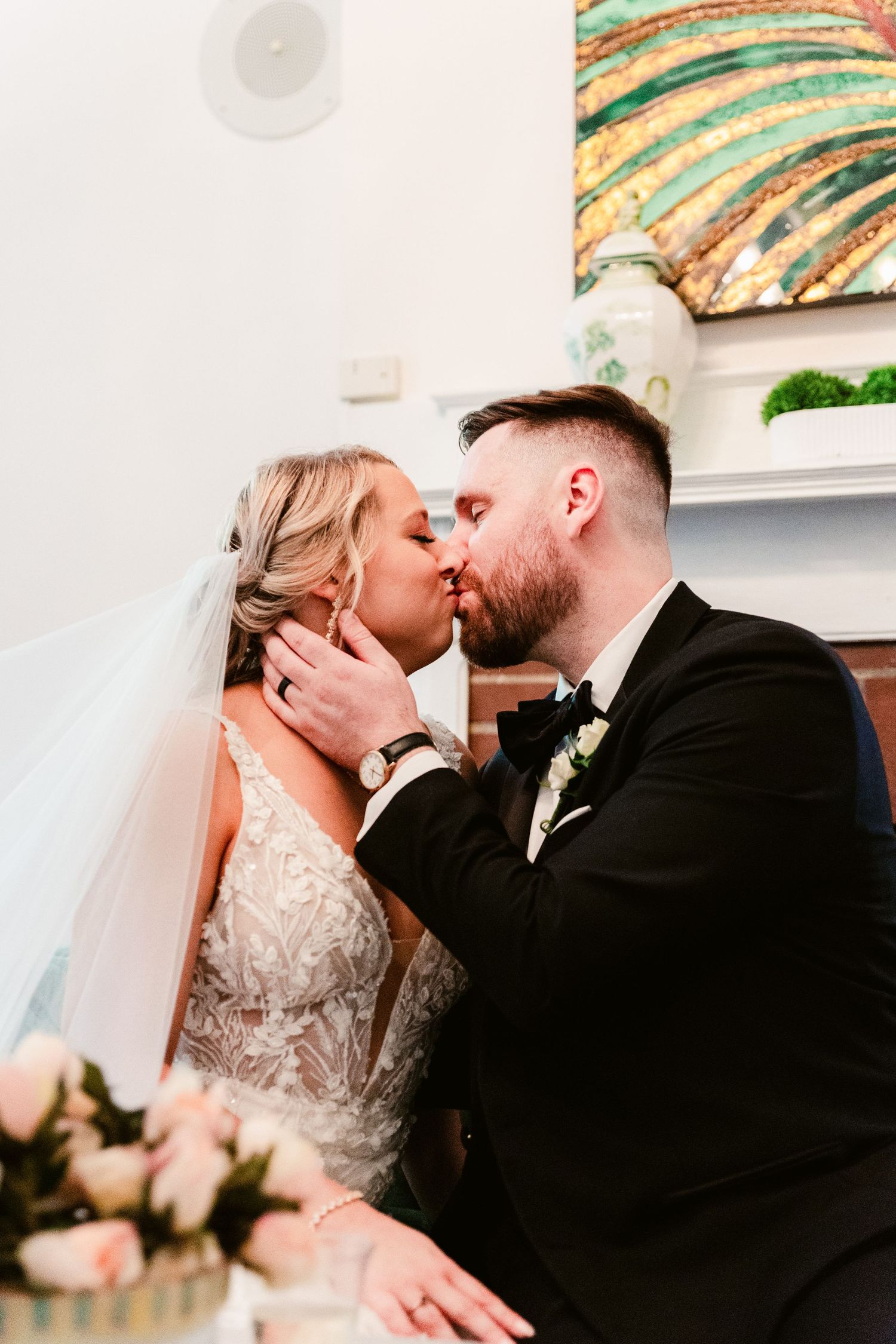 An intimate wedding moment captured indoors with decorative artwork visible on the wall.