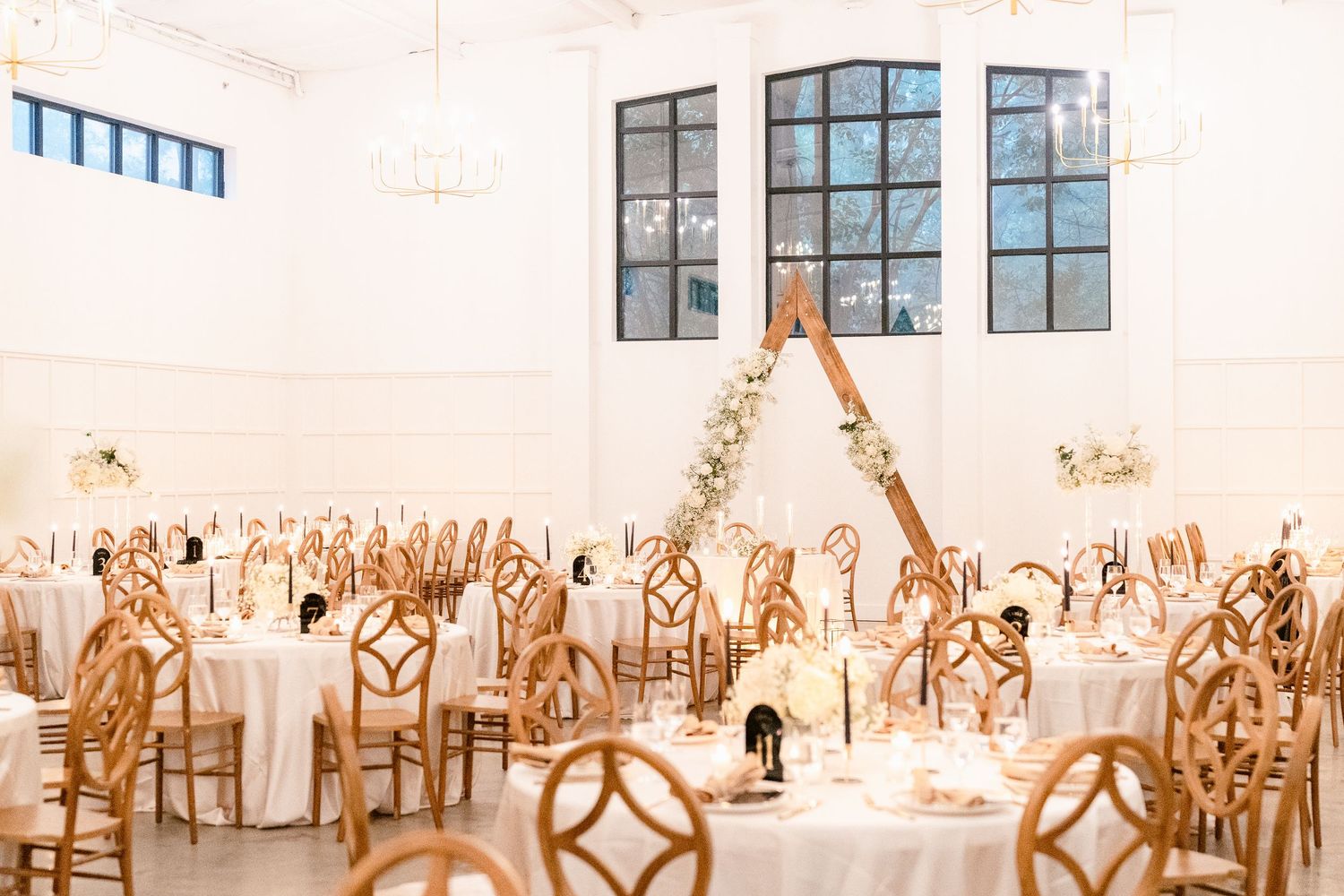 Light-filled wedding venue featuring modern gold geometric chairs and round tables set for an elegant reception.