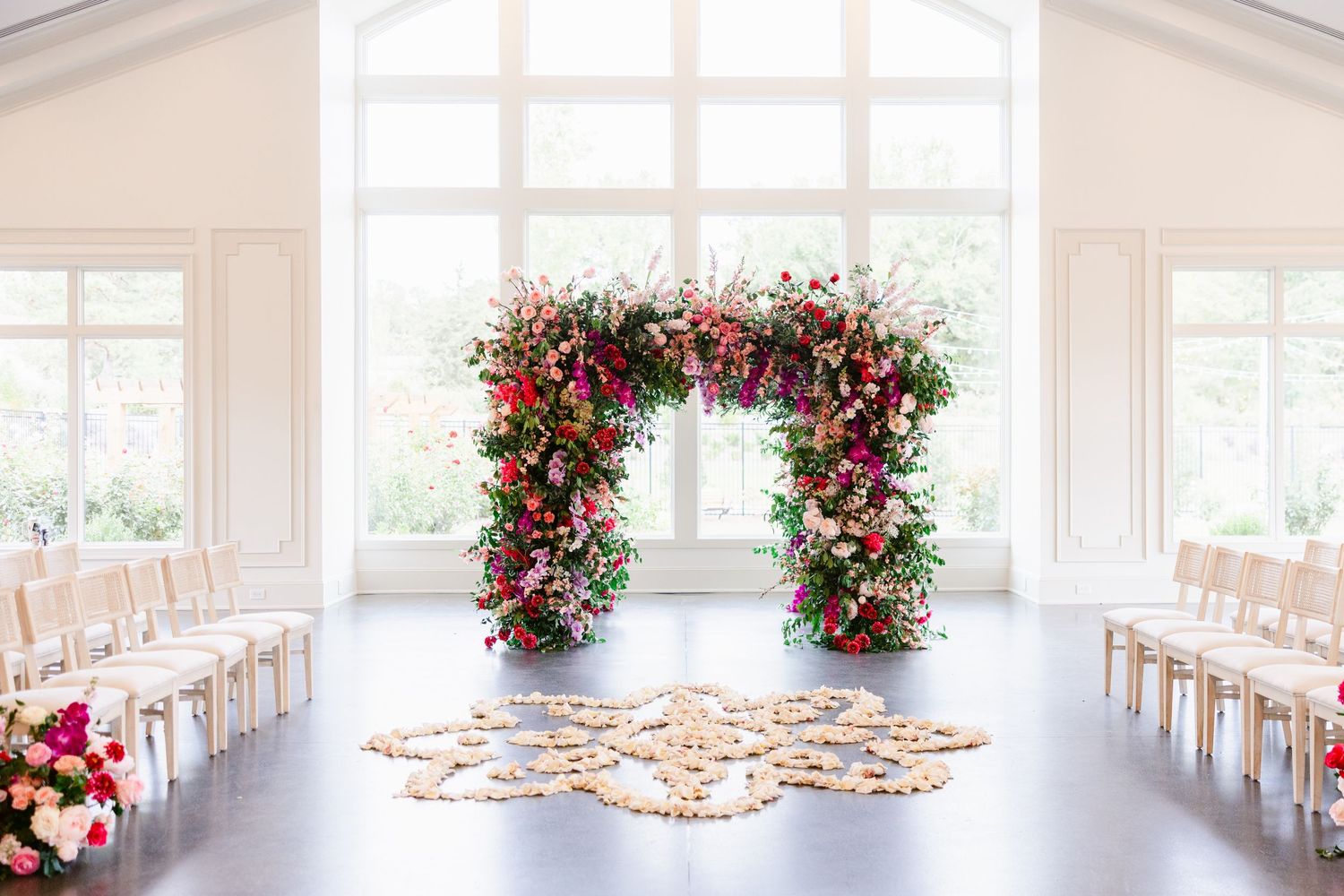 Bright white wedding venue with large windows and red floral arrangements along the aisle.