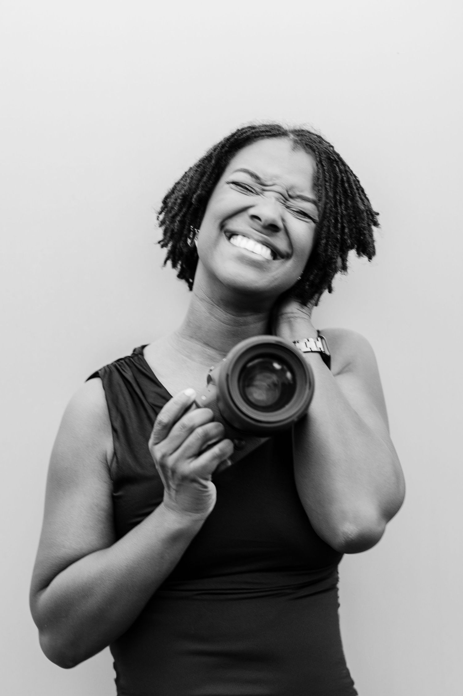 Black and white portrait of a joyful photographer with dreadlocks holding a camera while smiling brightly.