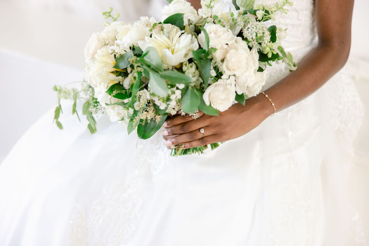 Romantic white floral bouquet with lush greenery and cream roses against a light background.