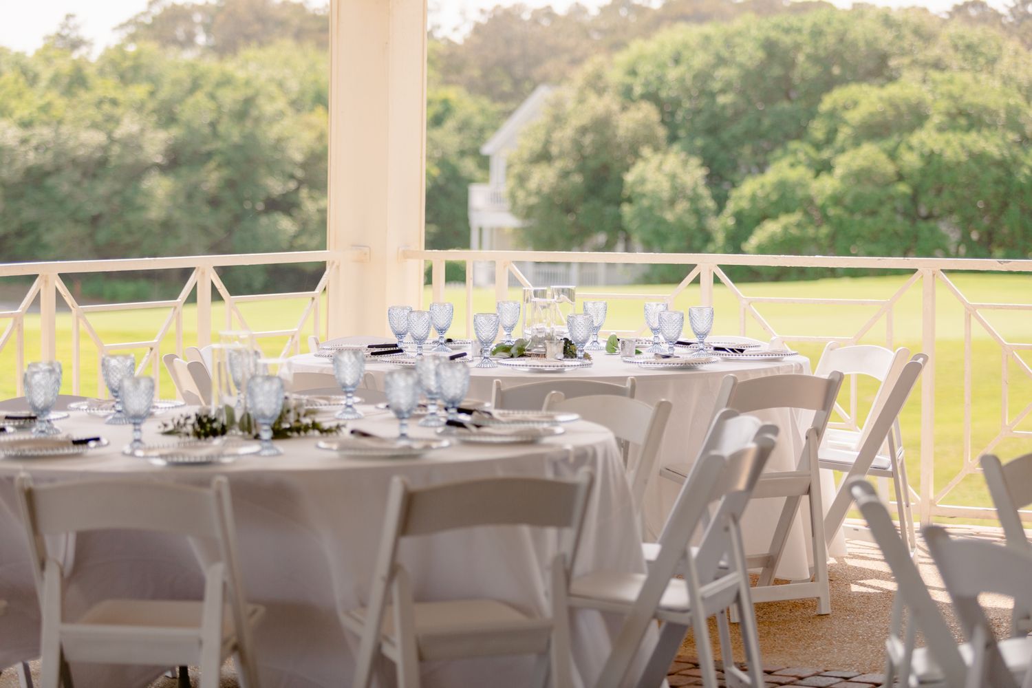 Elegant outdoor wedding reception tables set with white linens and chairs on a covered patio overlooking green fields.