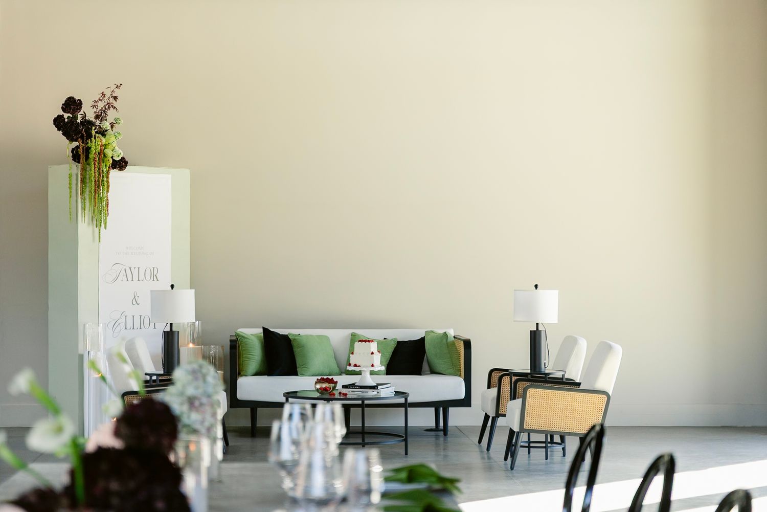 Modern dining room with minimalist white decor, black chairs, and hanging floral arrangements on long tables.
