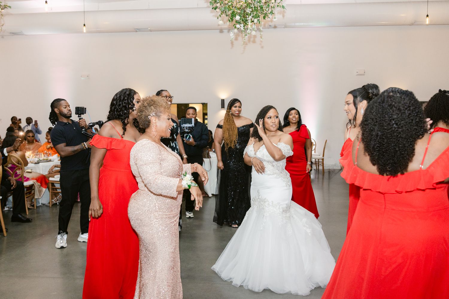 Wedding party members in red and white dresses dancing together at a modern reception venue.