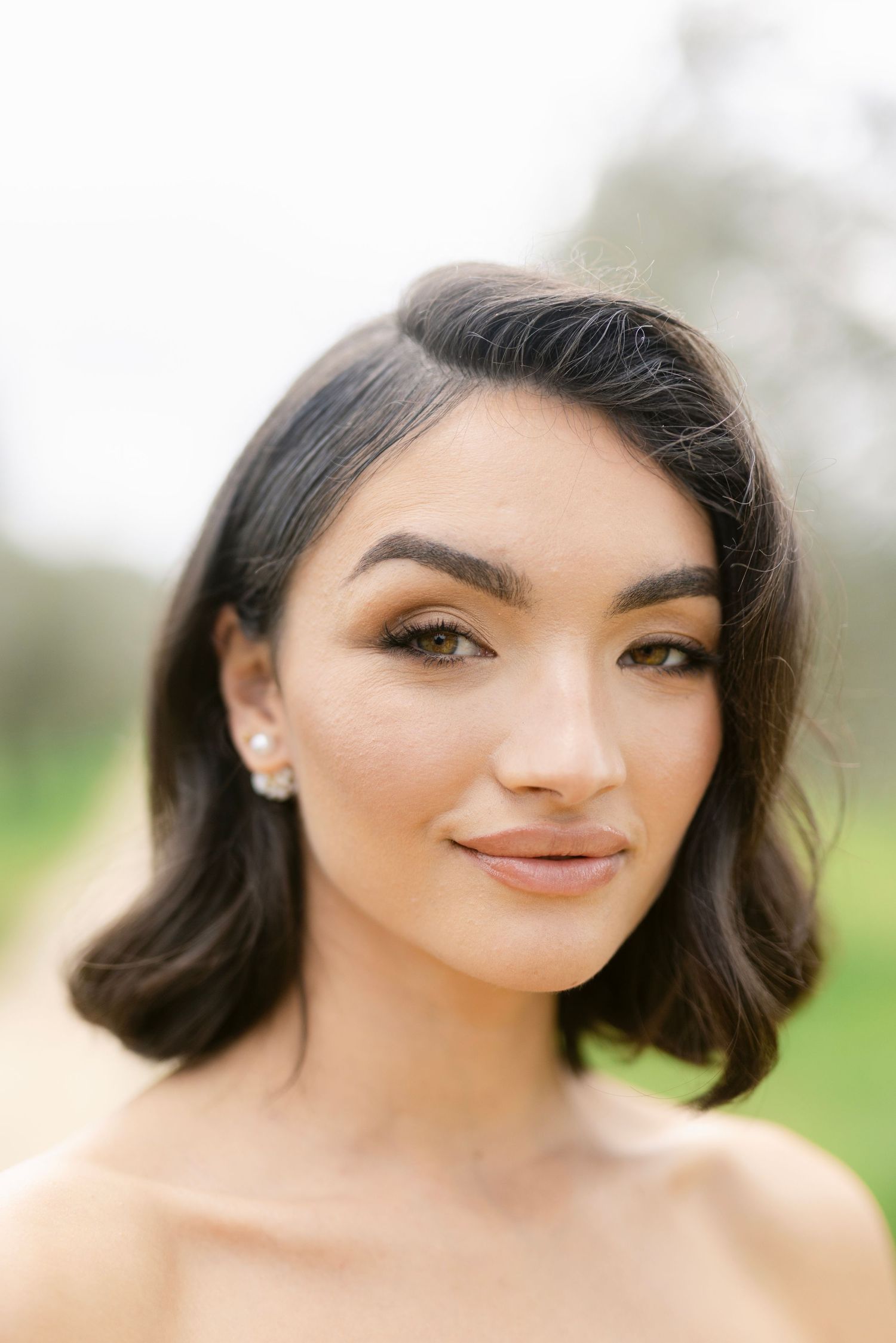 A close-up portrait showing elegant bridal makeup and styled dark hair against a soft natural background.