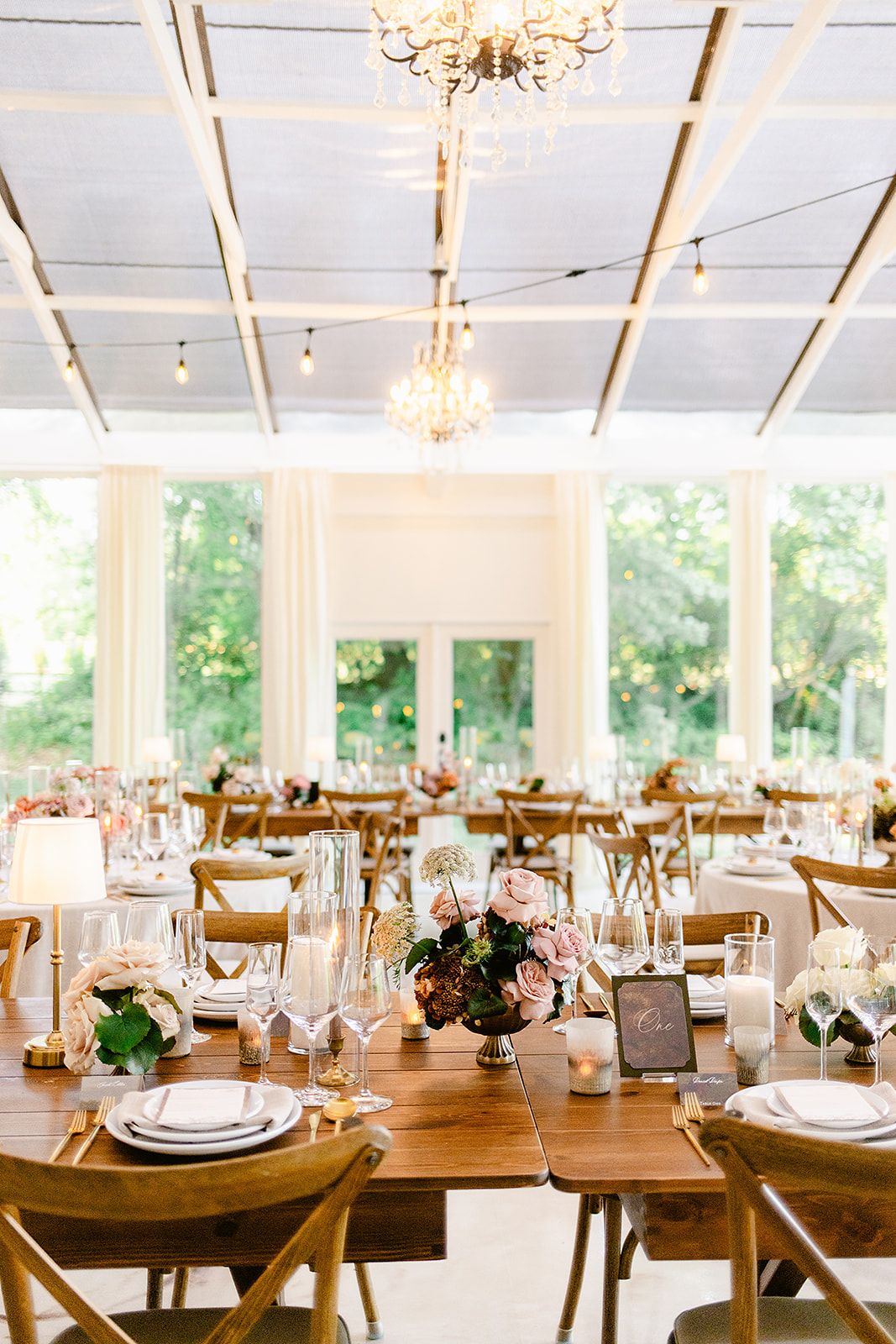 Rustic wooden farm tables set for a wedding reception with white place settings and delicate floral arrangements.