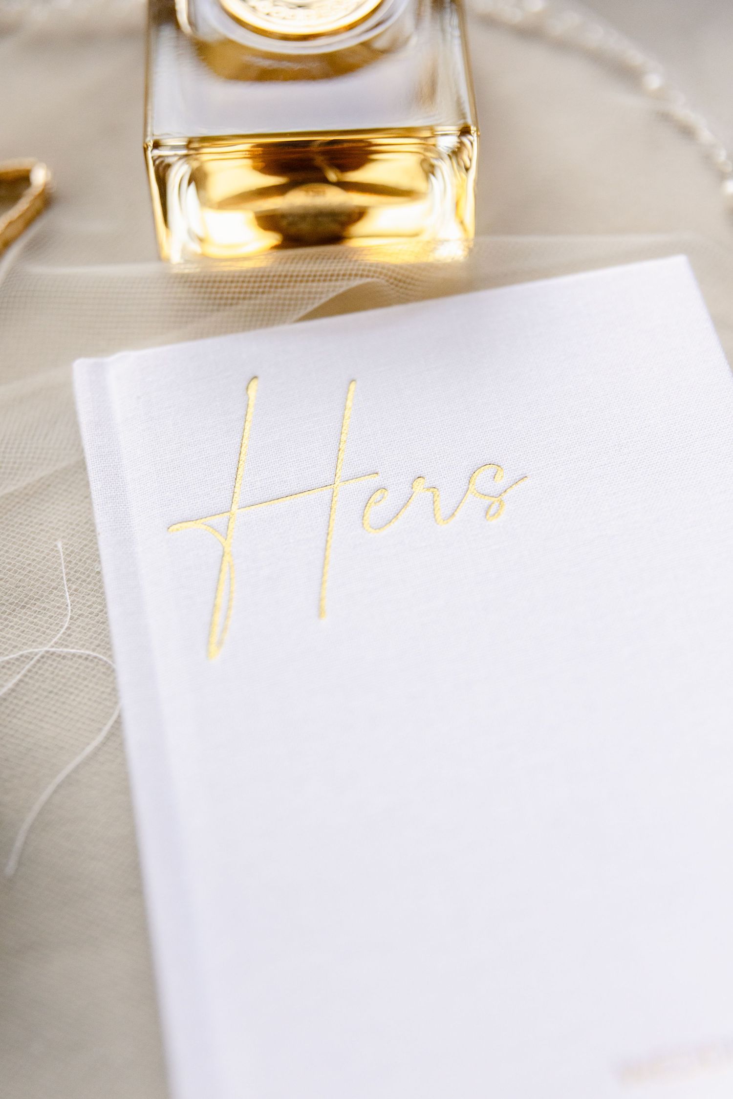 Close-up of white wedding stationery with gold 'Hero' text and perfume bottle.