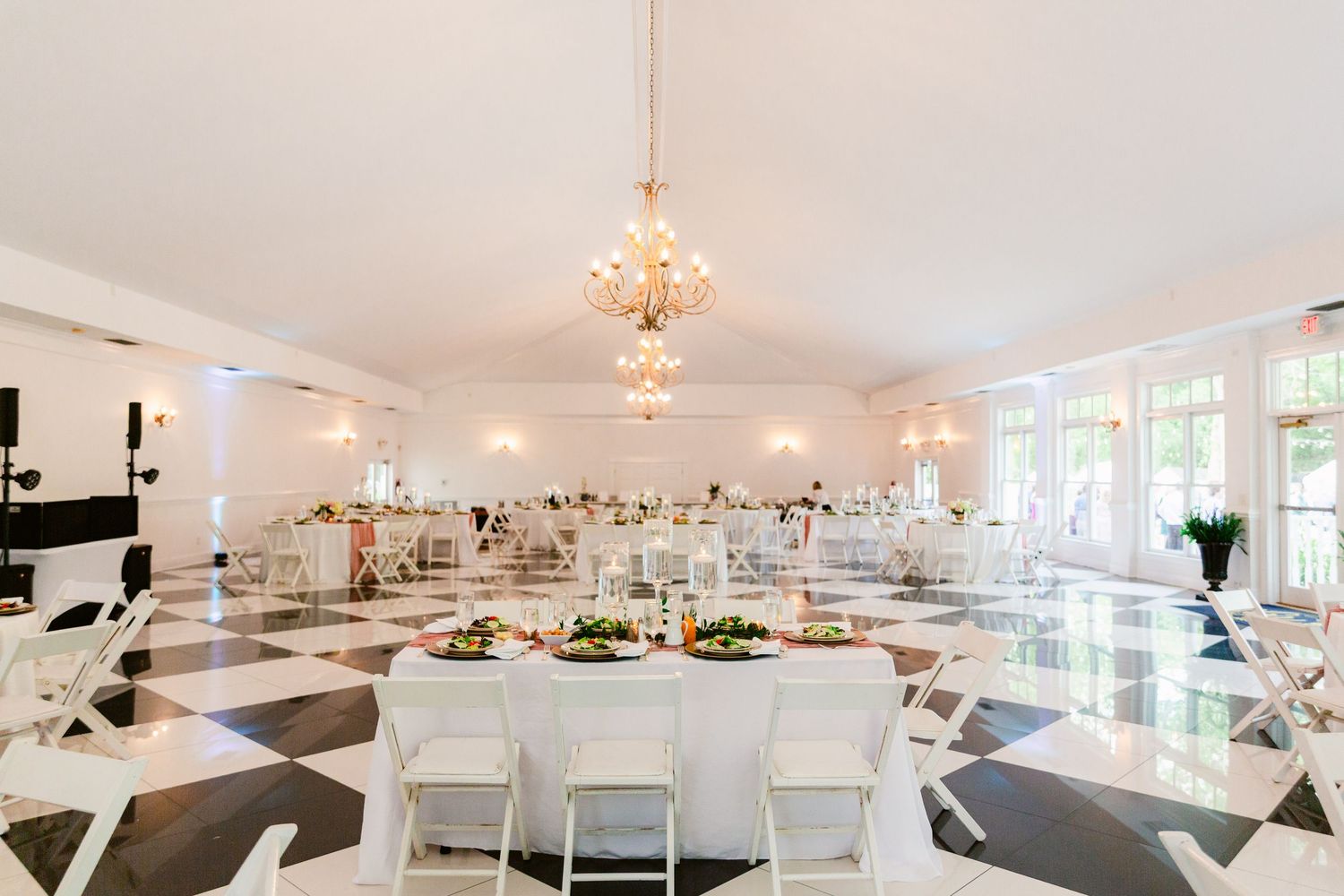 Elegant white wedding reception venue with crystal chandeliers and round tables set for a formal celebration.