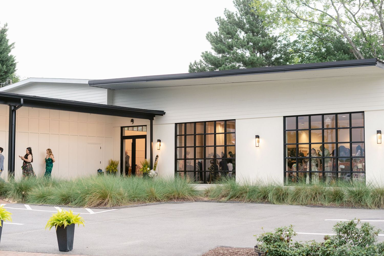 Modern white building exterior with large windows and landscaping features along a paved driveway.
