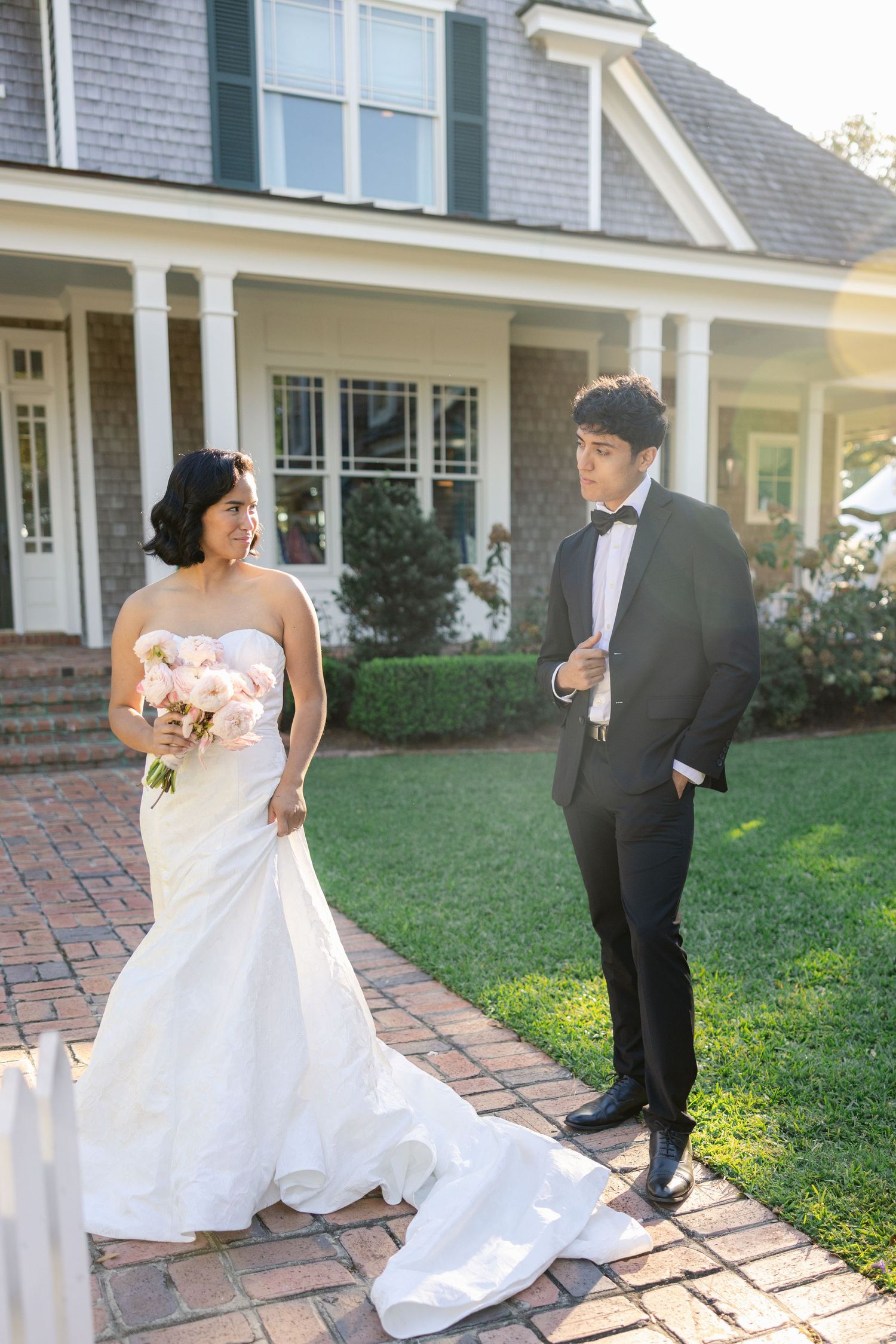 Elegant wedding scene on brick pathway outside classic coastal home.