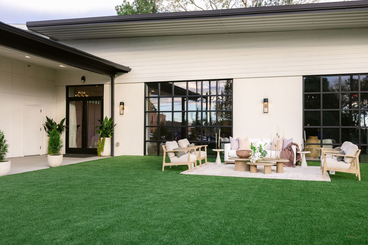 Modern white building exterior with floor-to-ceiling windows and green lawn landscaping creates a sleek architectural design.