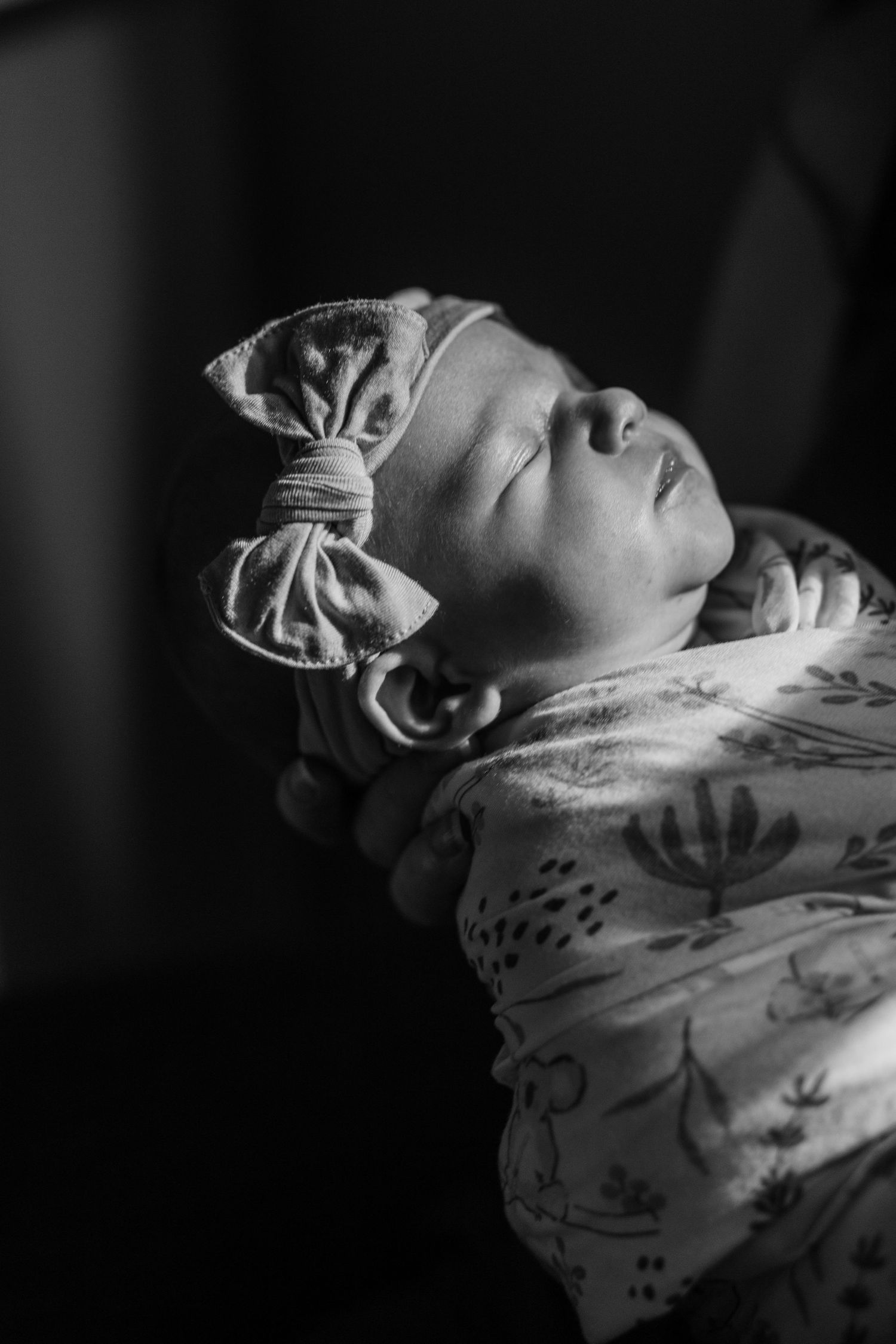 Artistic black and white close-up of a sleeping newborn swaddled in white fabric.