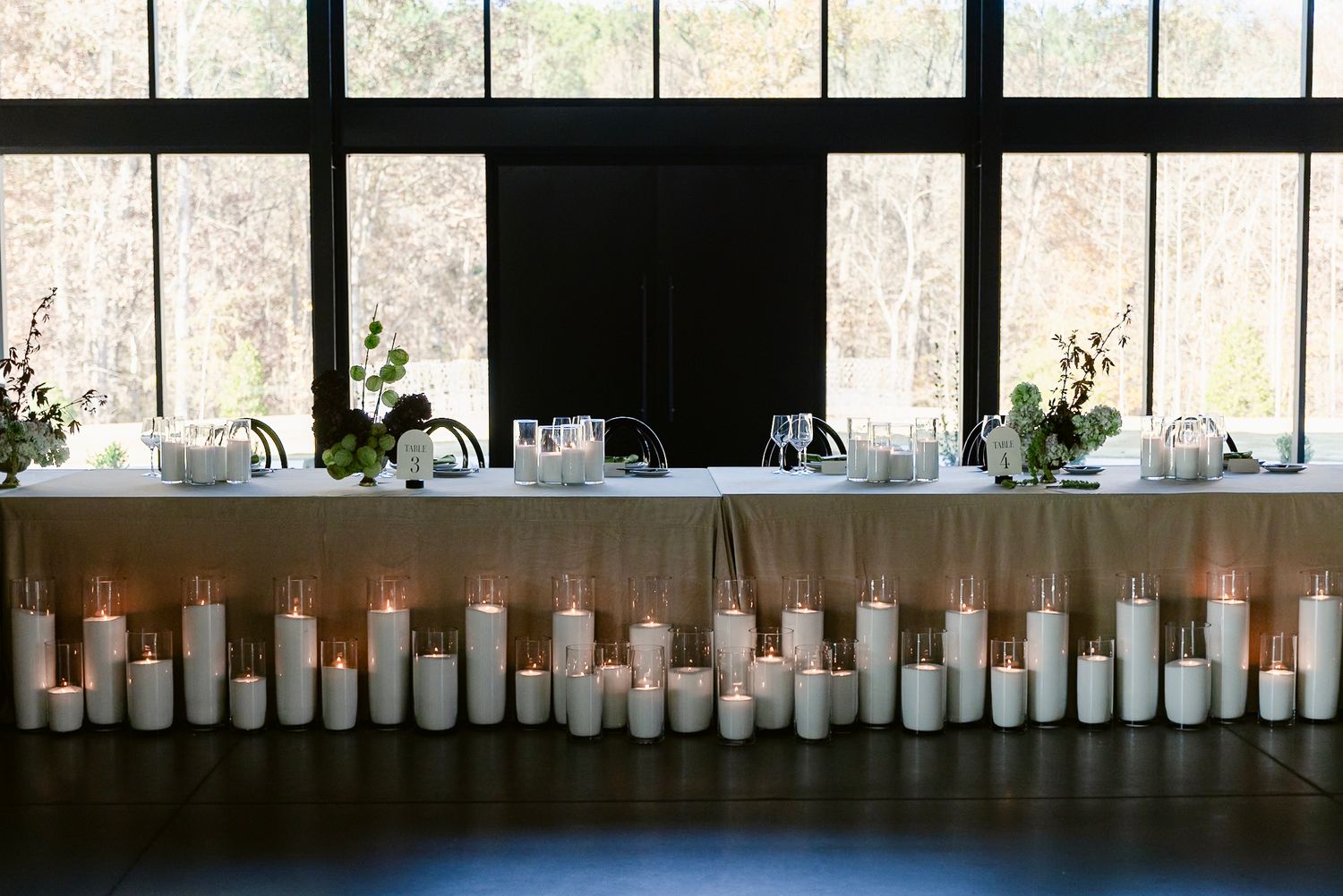 A row of white candles in glass holders line a window ledge creating an elegant wedding reception ambiance.