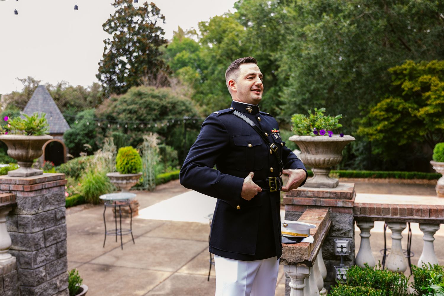 A person in a black jacket walks through a scenic garden path surrounded by lush greenery and stone walls.