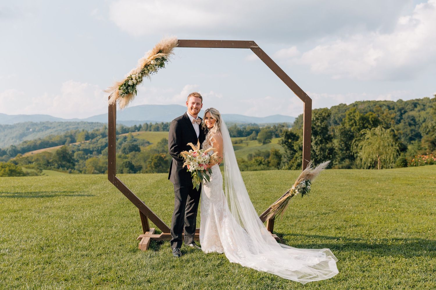 Wedding couple posing under a wooden octagonal arch in a scenic mountain setting.