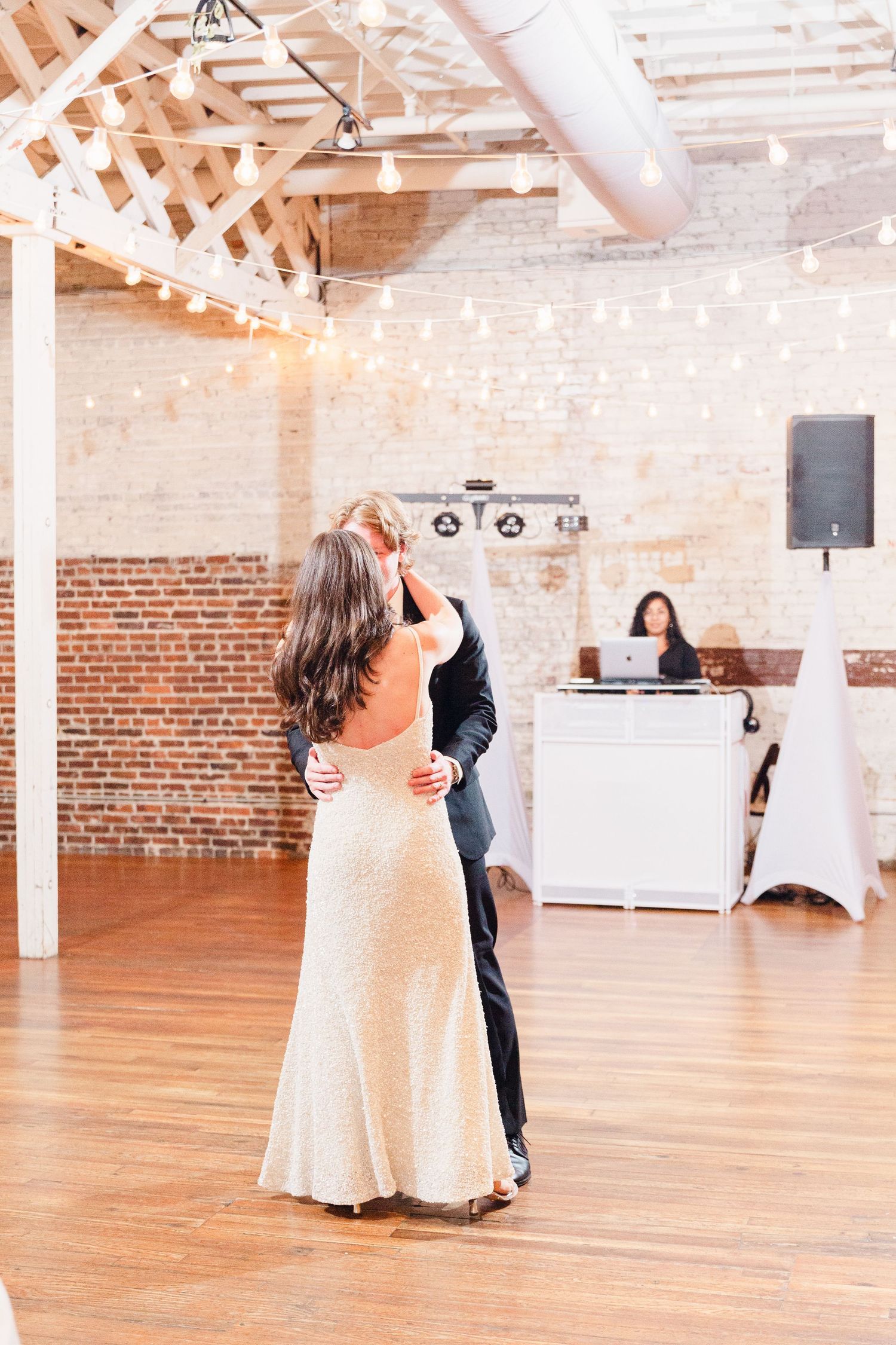 A couple shares their first dance in a rustic brick-walled venue with exposed beams and hardwood floors.