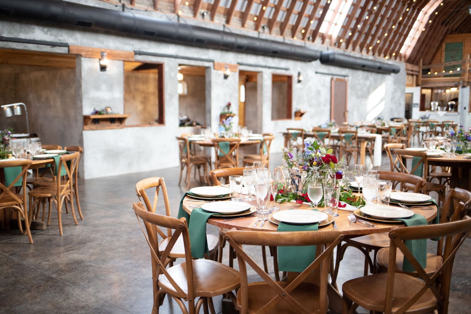 Wedding reception tables arranged in a rustic barn venue with wooden chairs and elegant place settings.