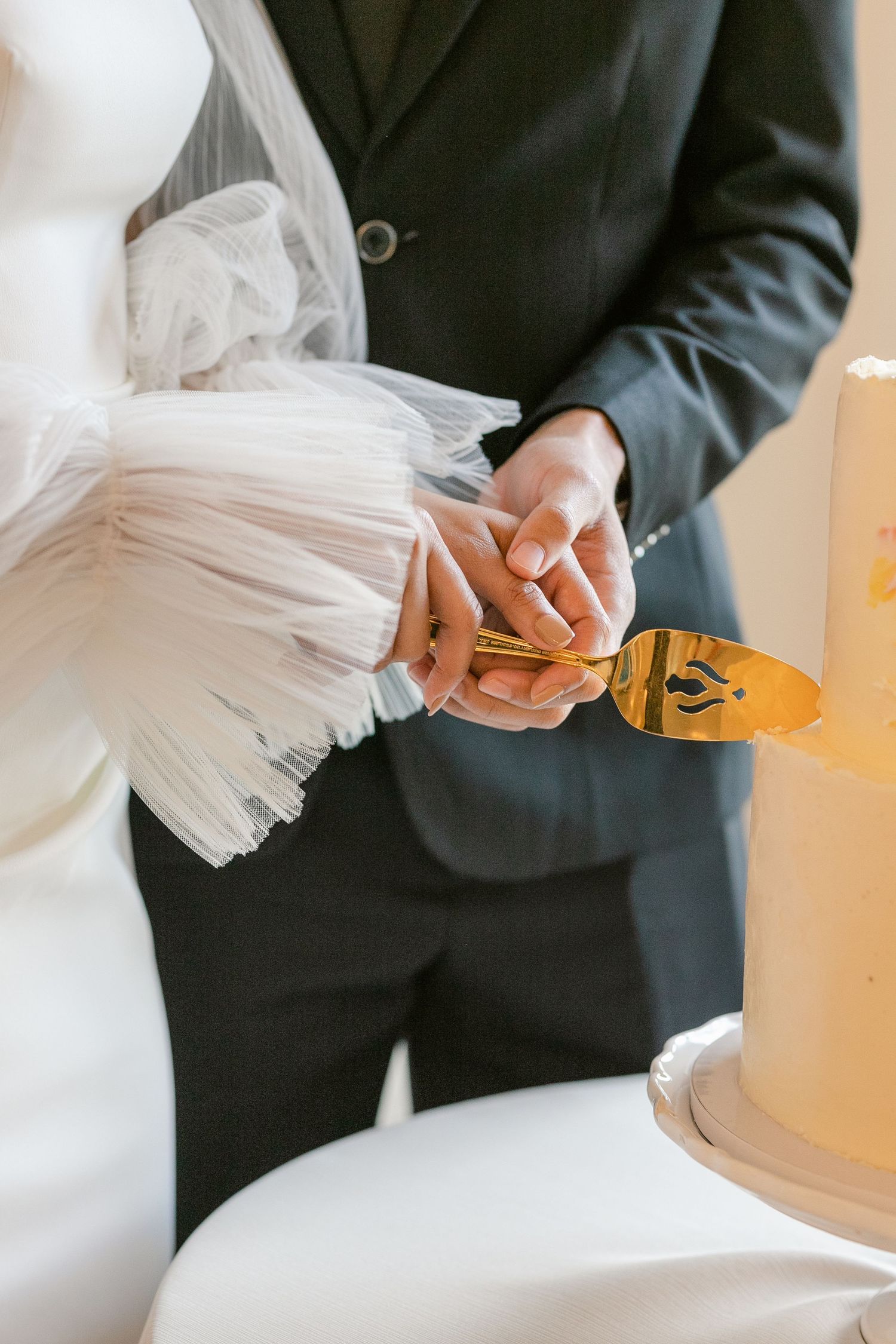 A couple in wedding attire cuts into an elegant yellow wedding cake with a gold serving knife.