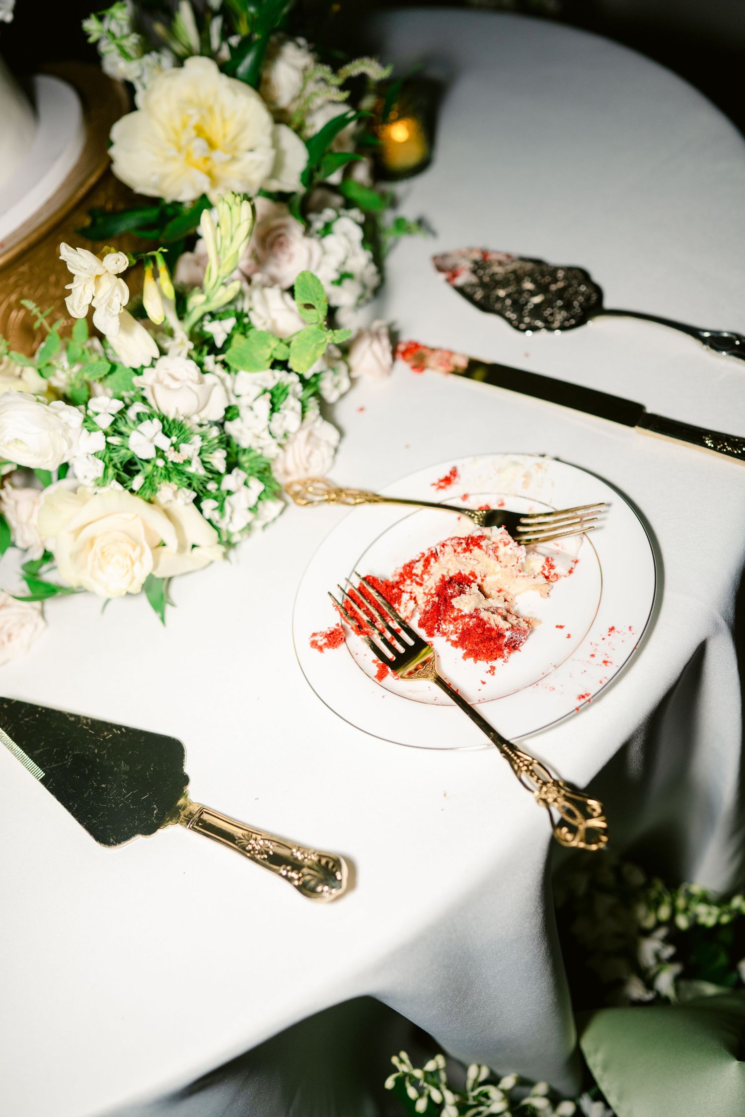 Elegant table setting with floral centerpiece and ornate silverware next to a plate with red sauce remnants on white linen.