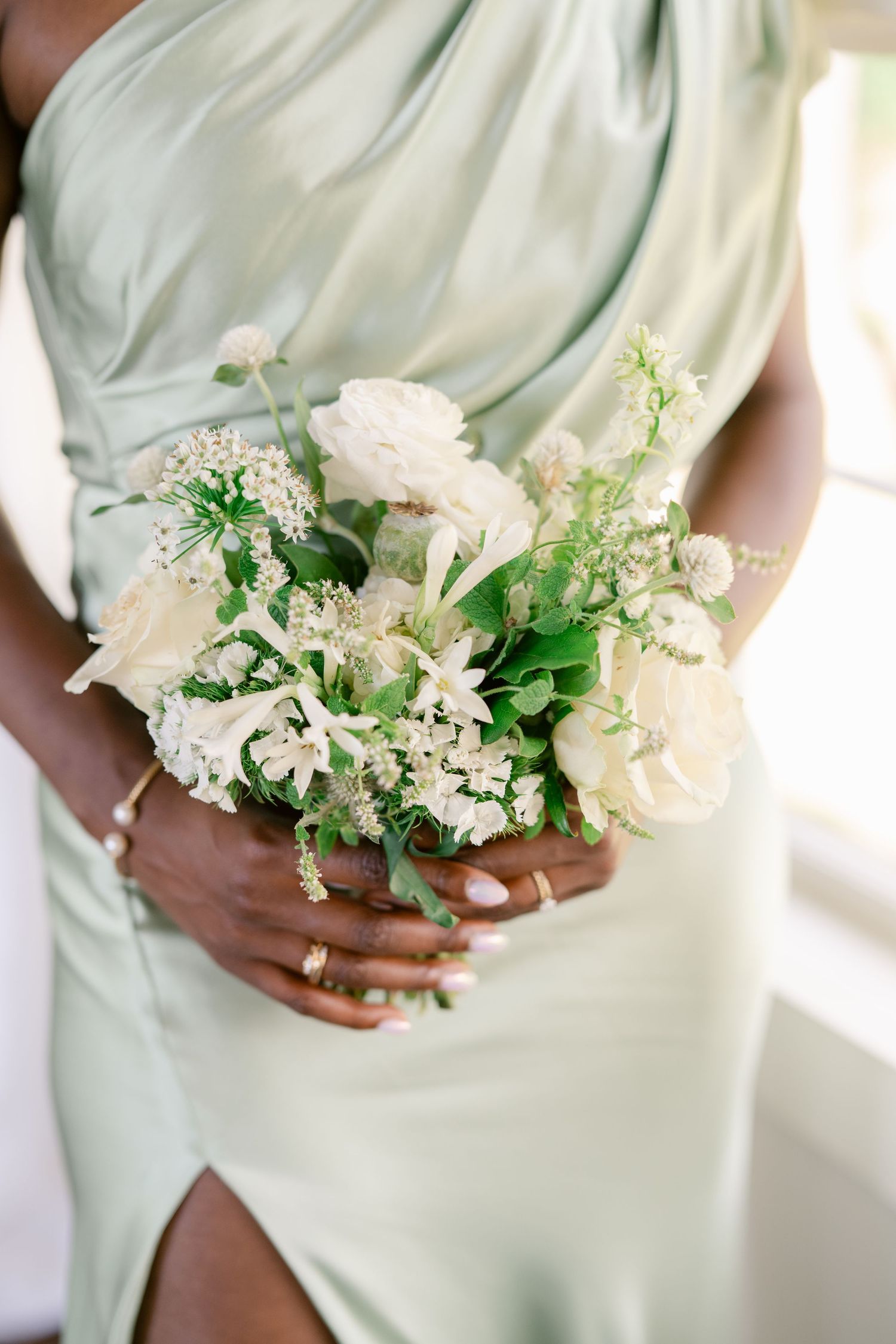 Bridesmaids in sage green dresses holding white and green floral bouquets.