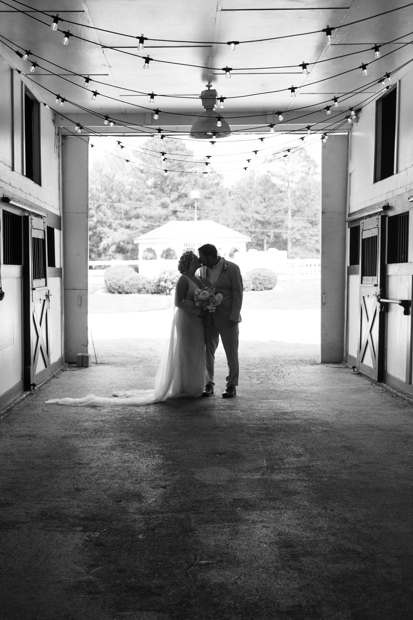 A romantic silhouette under string lights in a barn doorway, captured in black and white photography.