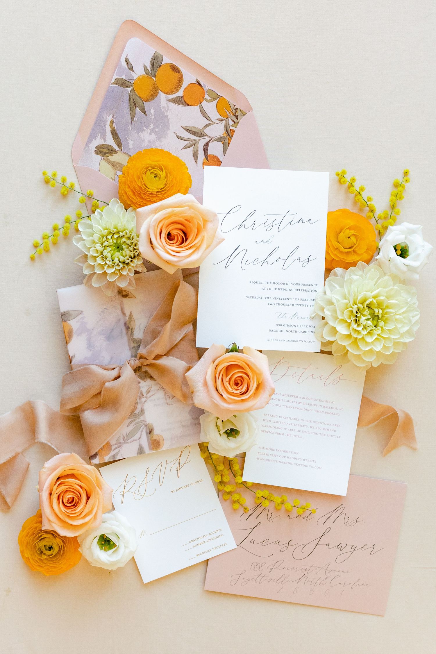 Wedding stationery with peach and orange roses, ranunculus flowers, and calligraphy on a light marble background.