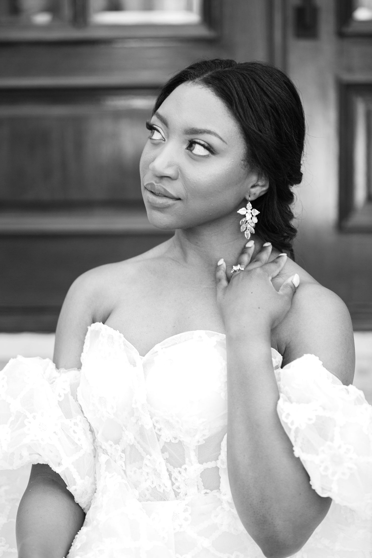 A bride in a white wedding dress with floral details gazes elegantly to the side in a black and white photo series.
