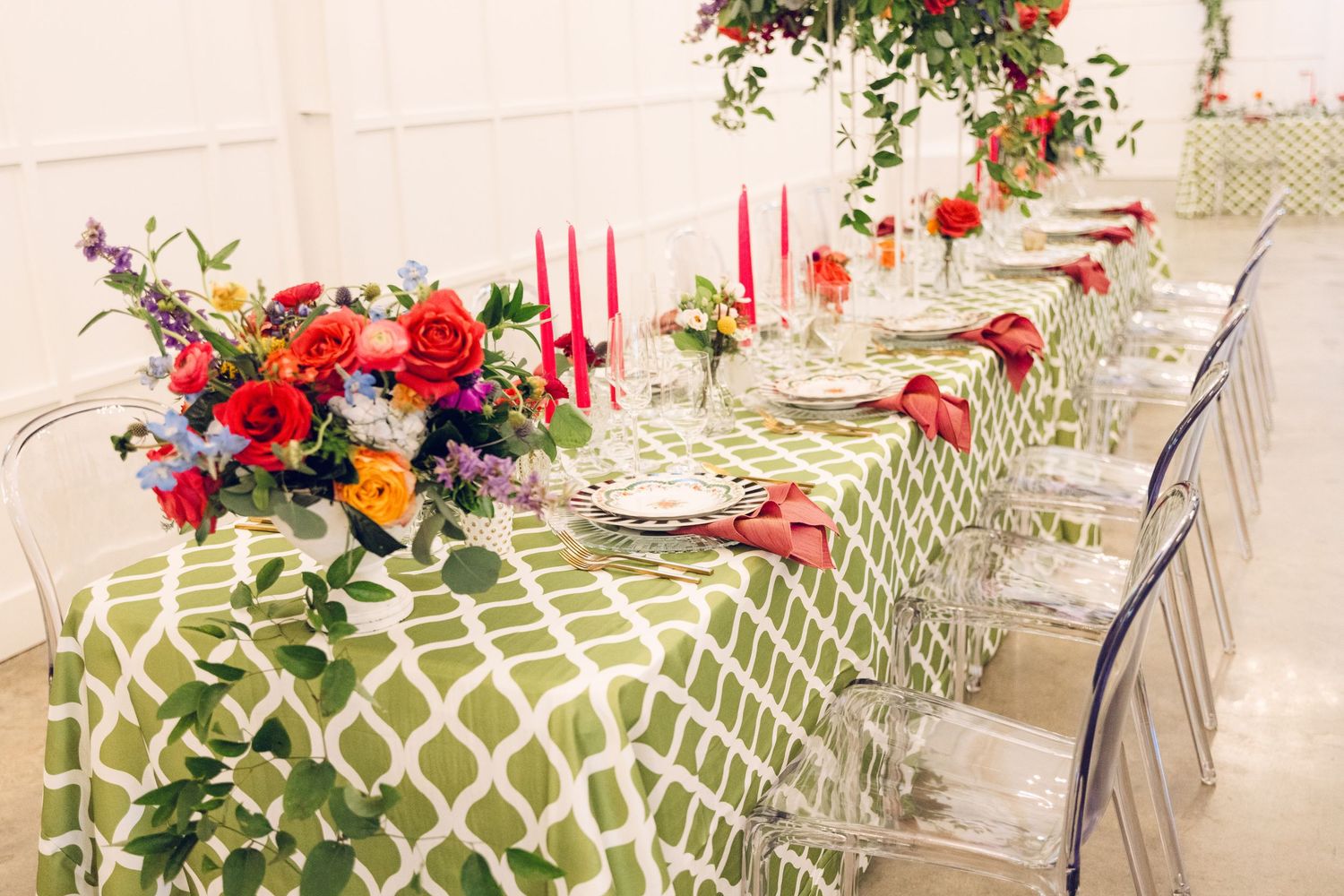 Rustic outdoor porch decorated with red and orange flowers in hanging baskets and white wicker furniture.