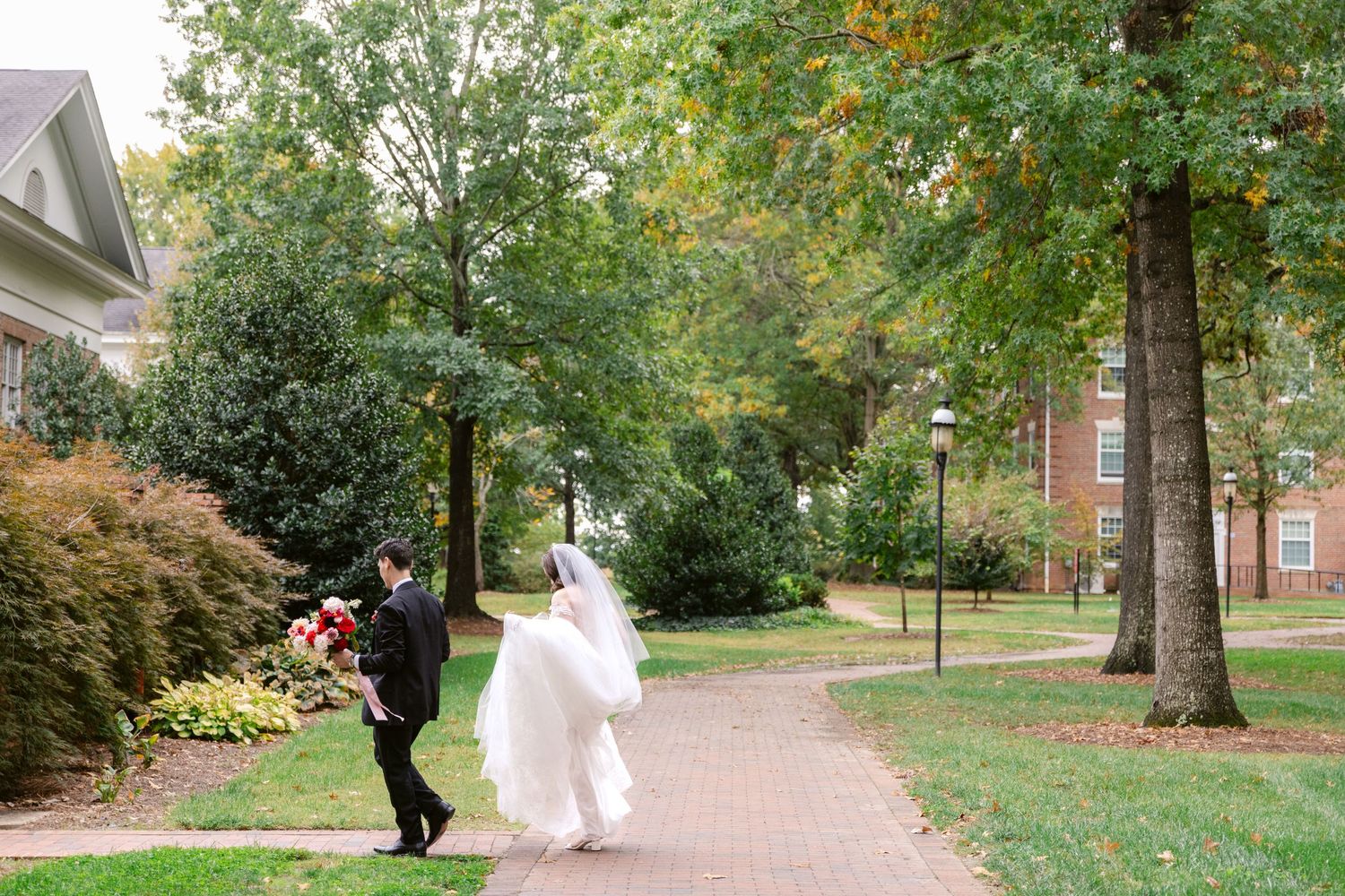 A couple walking along a brick pathway surrounded by autumn trees and landscaping on a college campus.