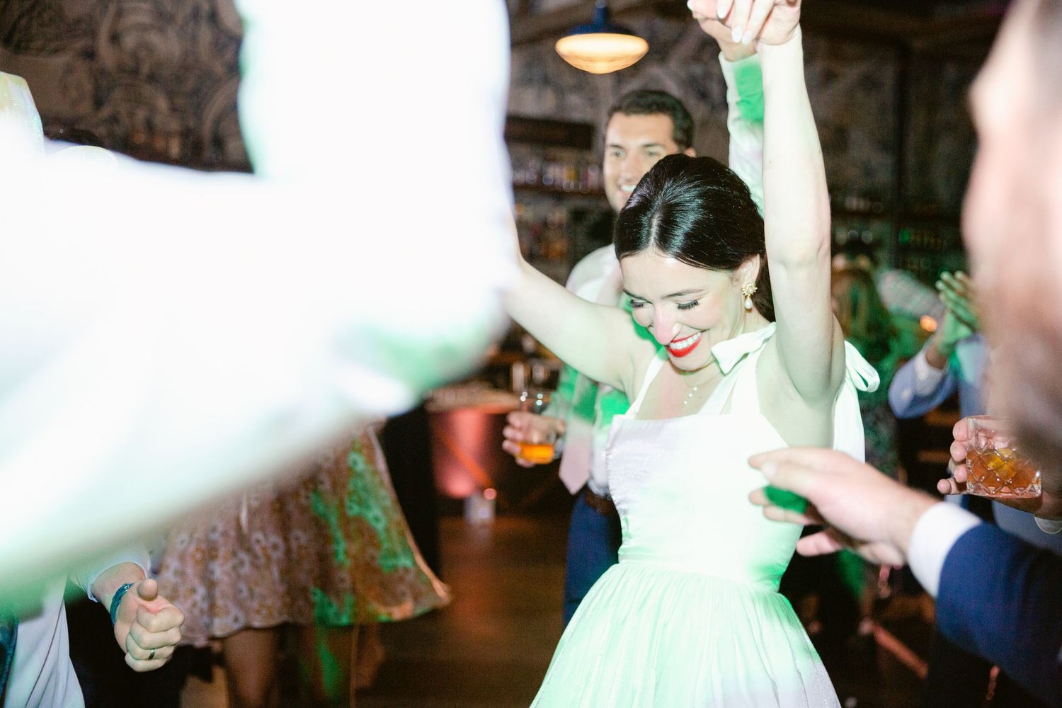 Wedding guests dancing and celebrating on a dimly lit dance floor at a reception party.