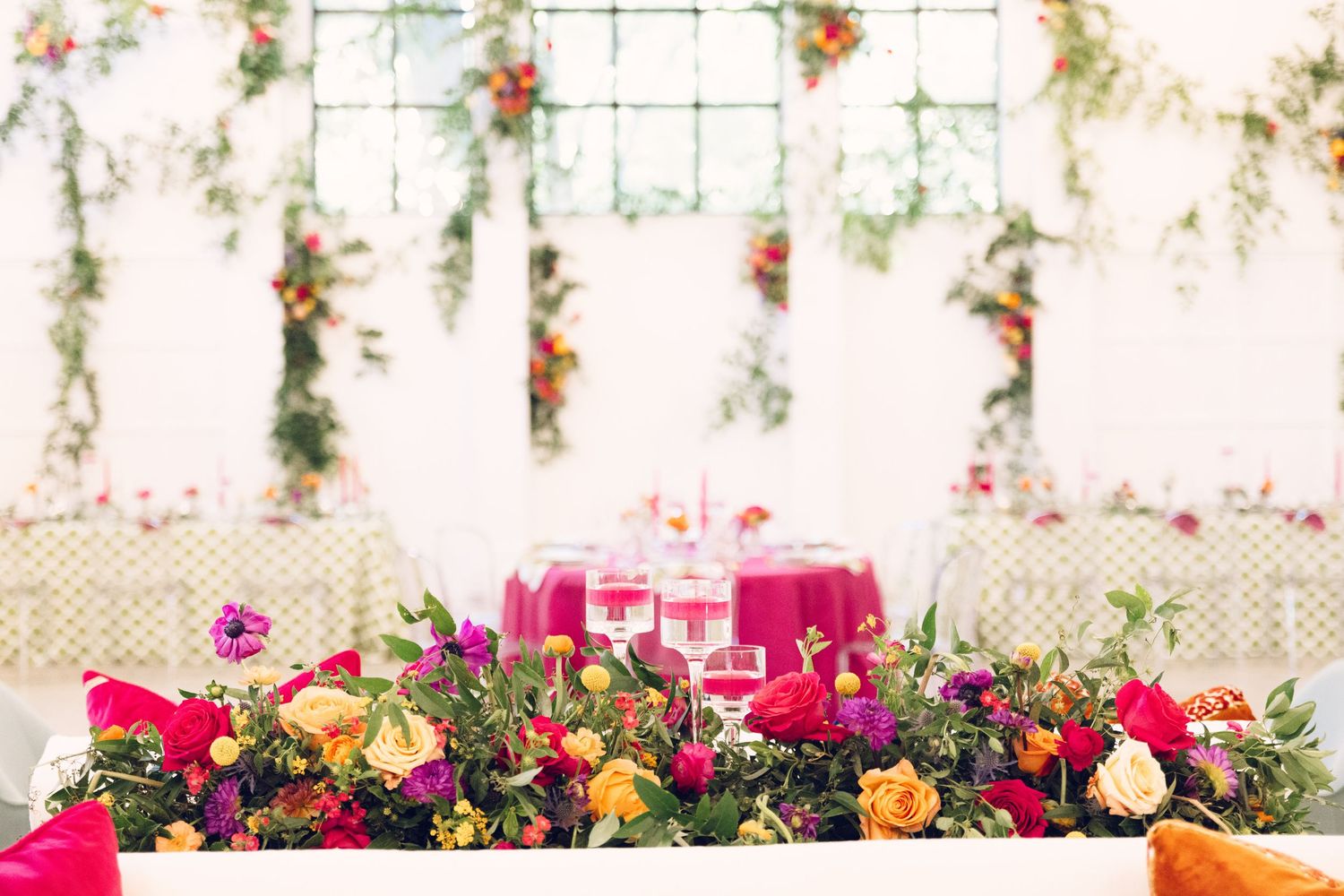 Colorful floral installations and greenery decorate windows in a light-filled event space.