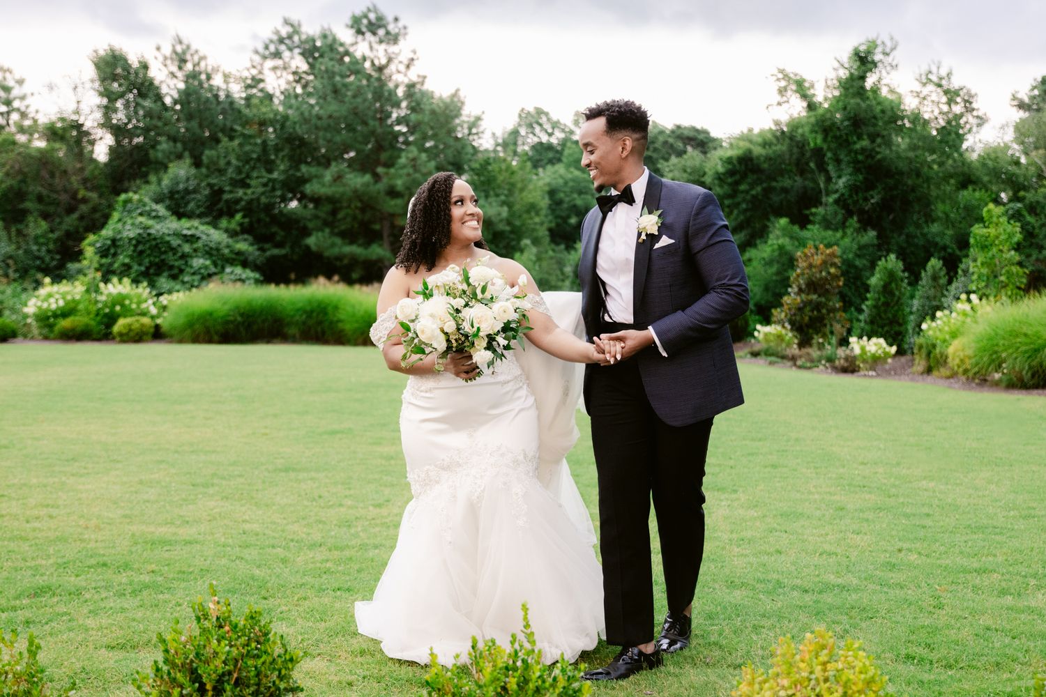 A couple in wedding attire shares a romantic moment in a lush green meadow with wildflowers.