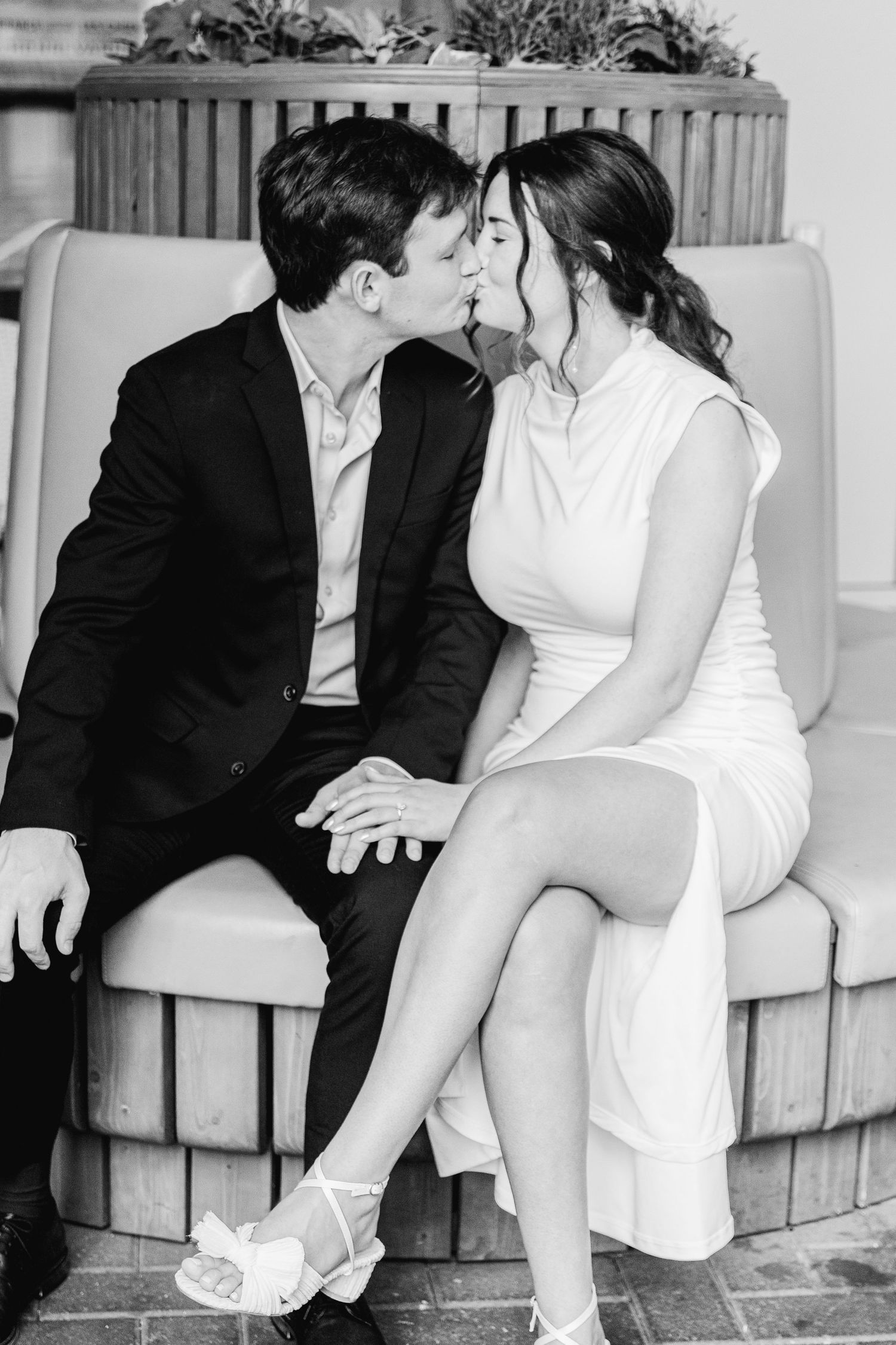 A romantic black and white photo of a couple sharing an intimate moment while sitting together on an upholstered bench.