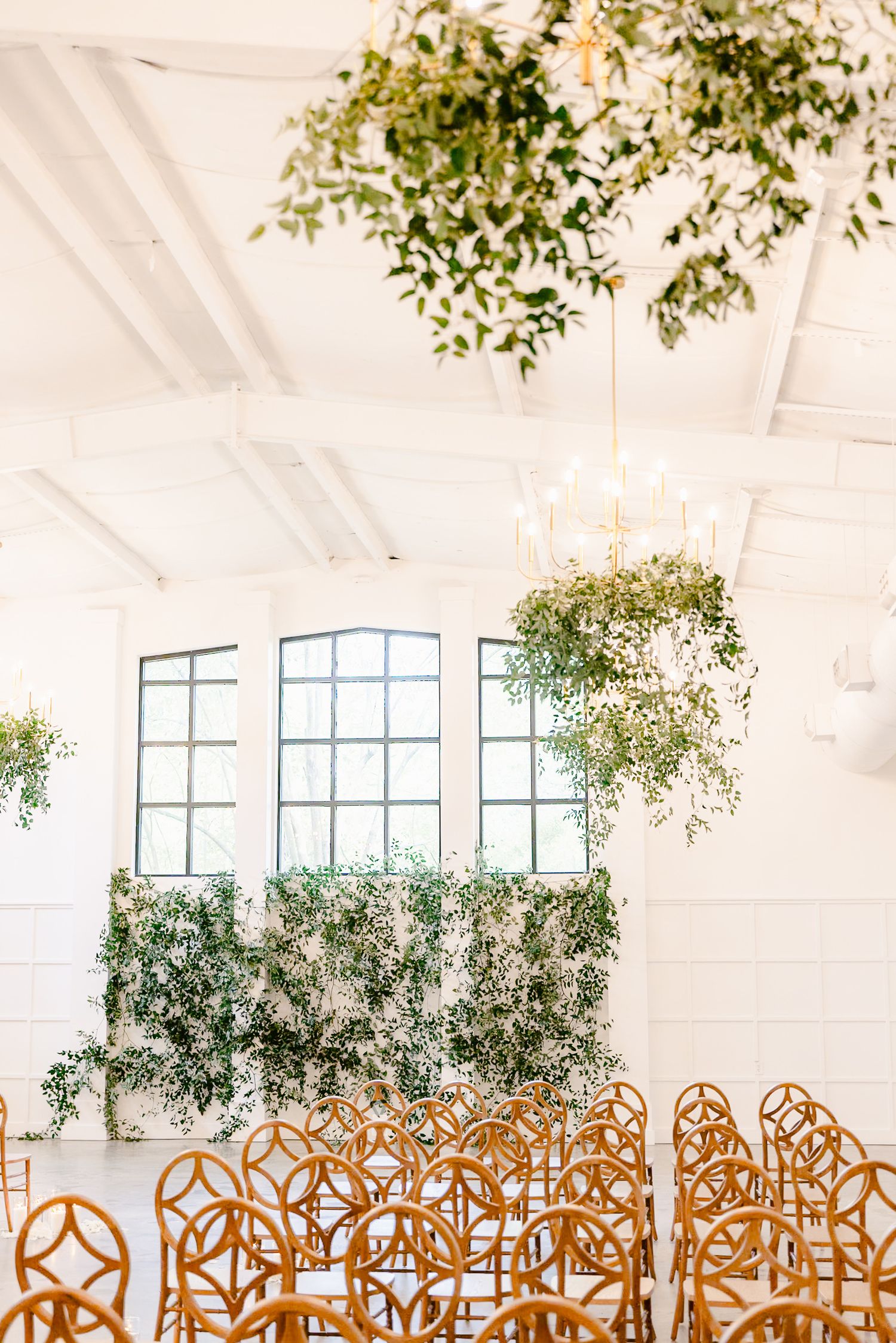 Elegant white wedding reception venue with hanging greenery and rows of copper-colored chairs arranged for a ceremony.