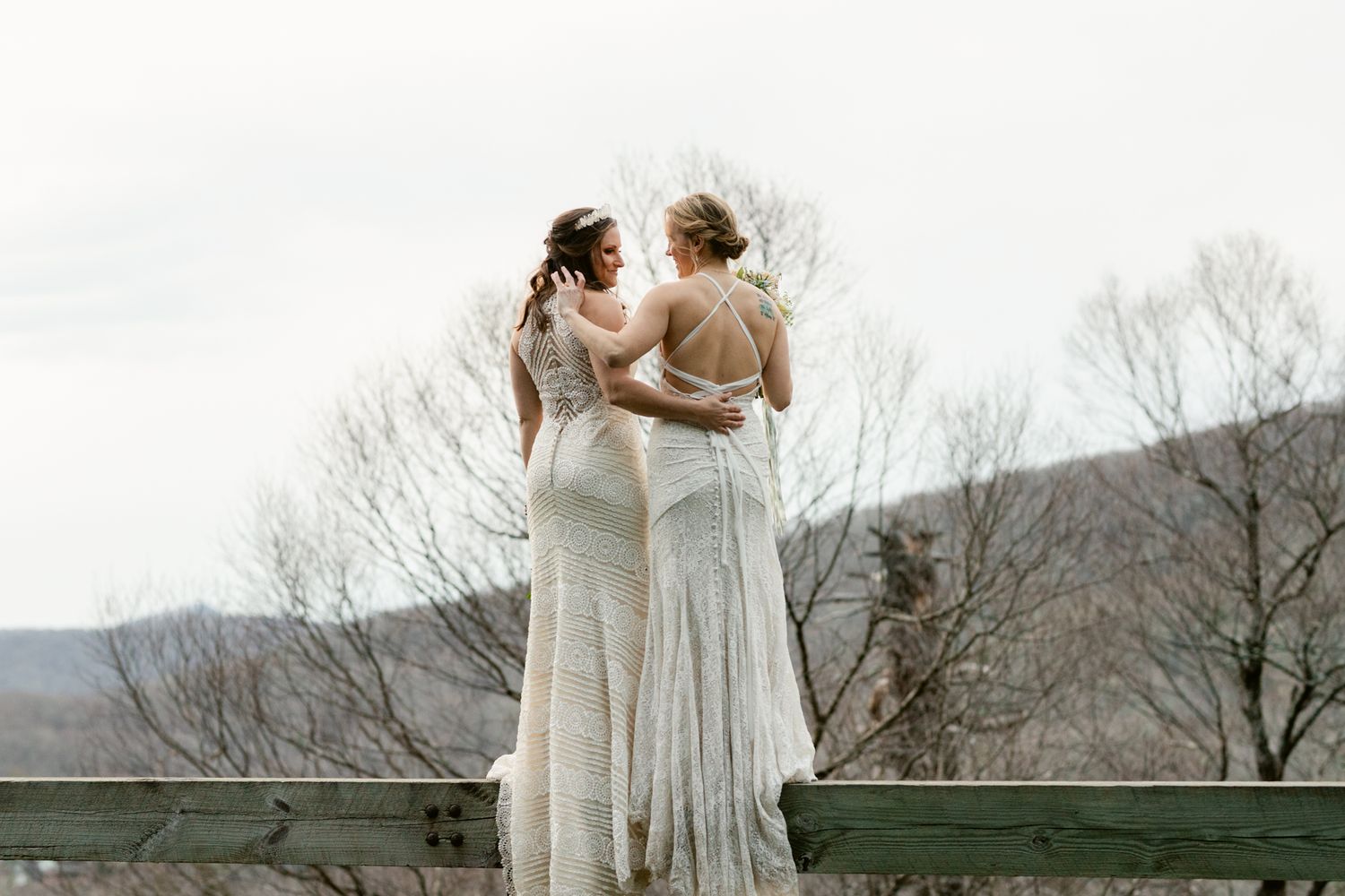 A romantic moment between two people in flowing white dresses against a mountain backdrop.