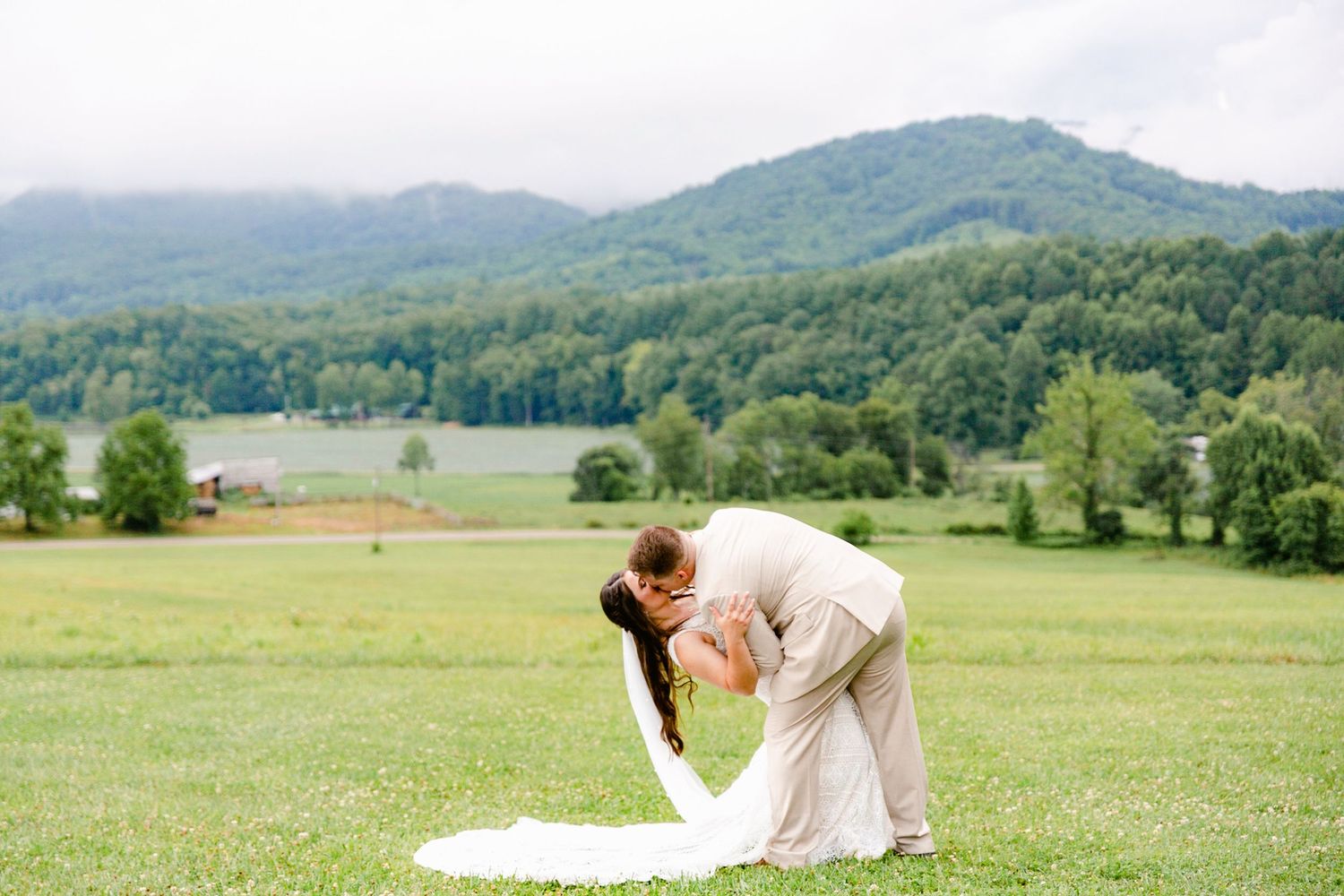 Rolling green hills and mountains create a scenic backdrop for an outdoor wedding ceremony in a lush meadow.