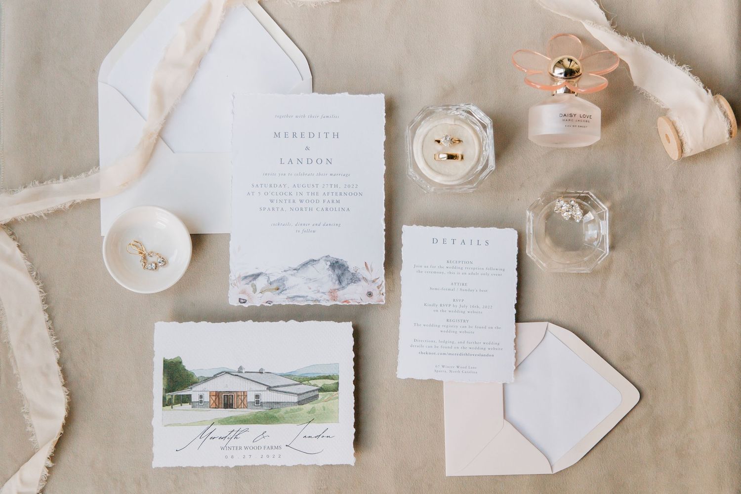 Wedding invitation suite with floral details and watercolor venue illustration laid out on neutral fabric.
