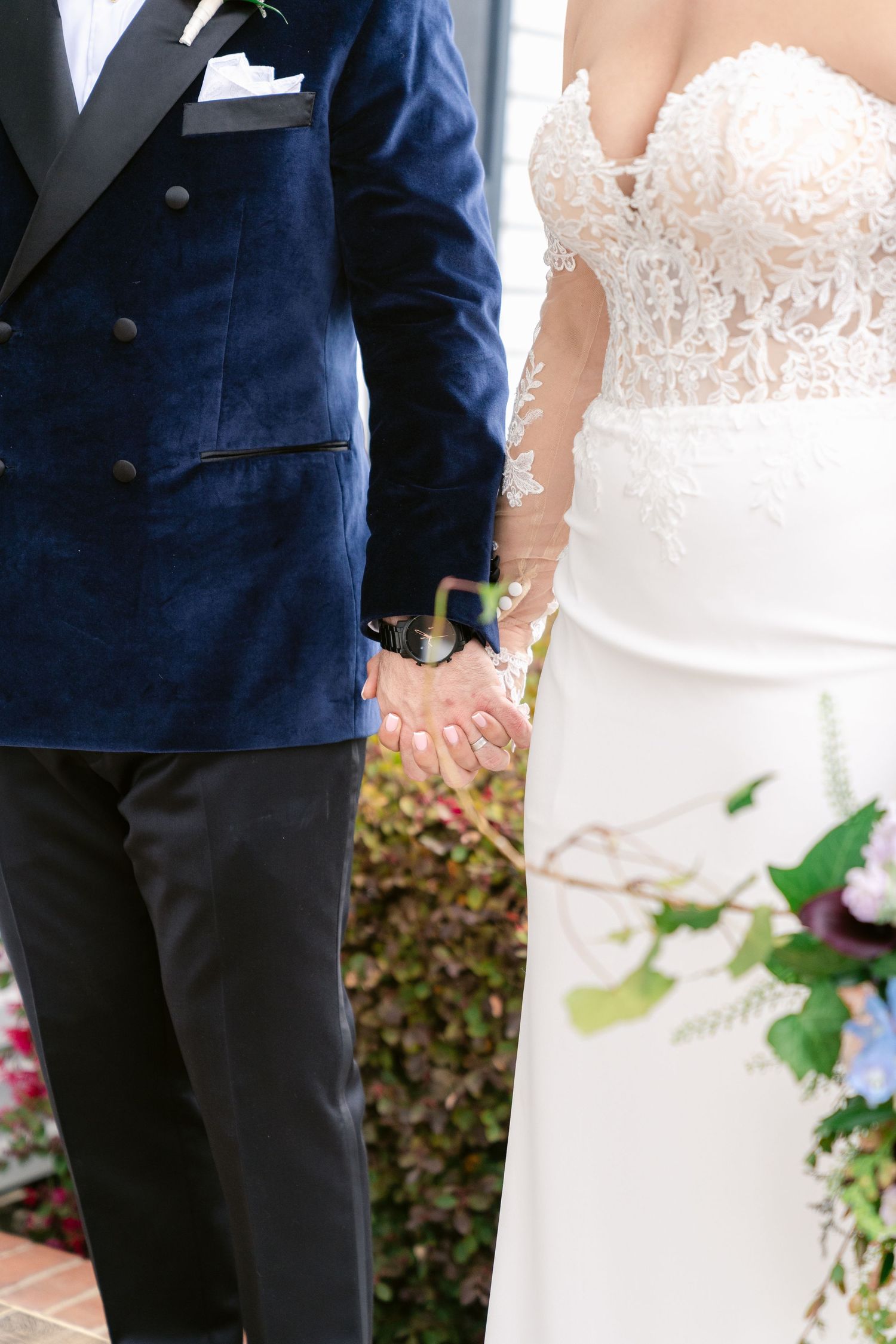 Close-up of couple in navy suit and white lace wedding dress holding hands.