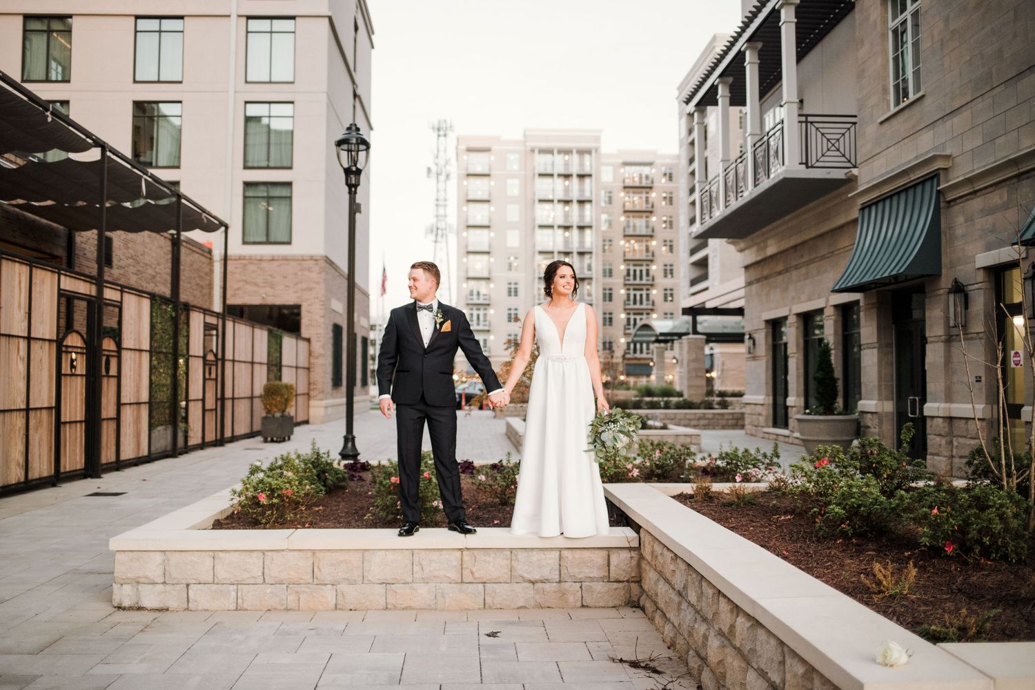 Newlyweds stand together on garden terraced steps in urban setting.