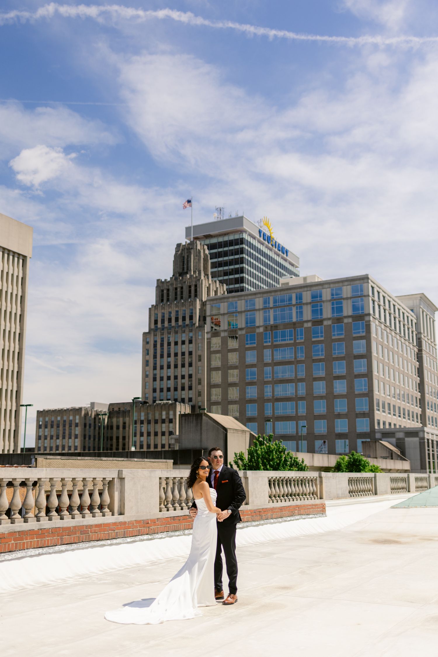 Bride and groom pose on urban rooftop with city skyline backdrop on their wedding day.