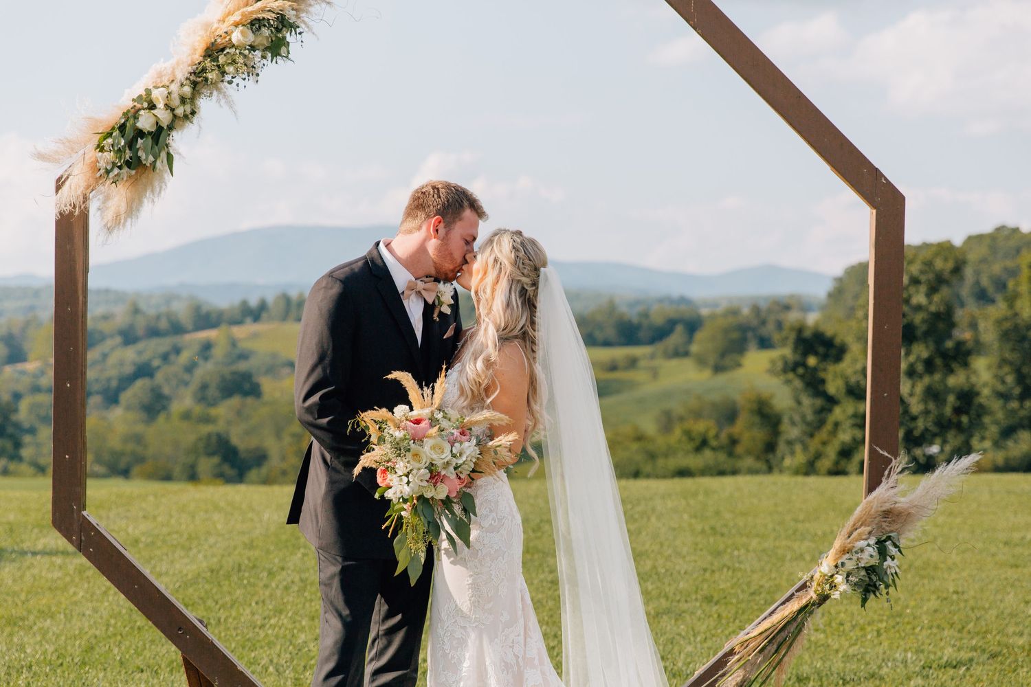 Romantic wedding portrait under geometric wooden arch with mountain landscape backdrop.