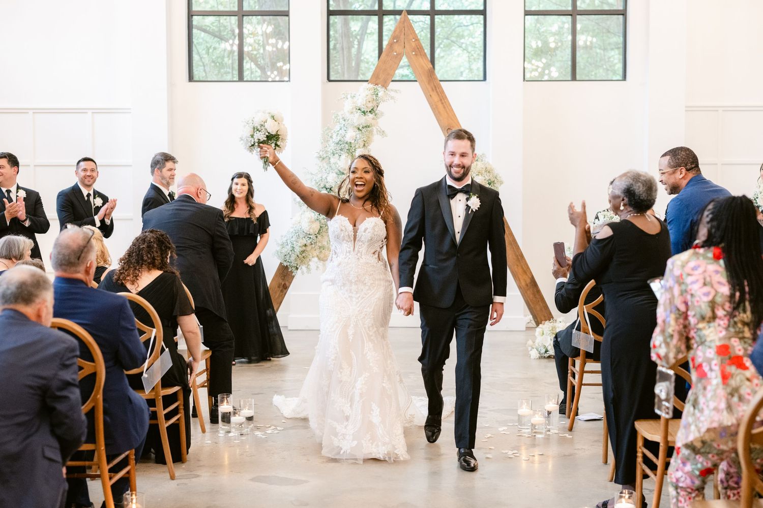 Newlyweds joyfully walk down the aisle together while wedding guests celebrate in a bright, elegant chapel venue.