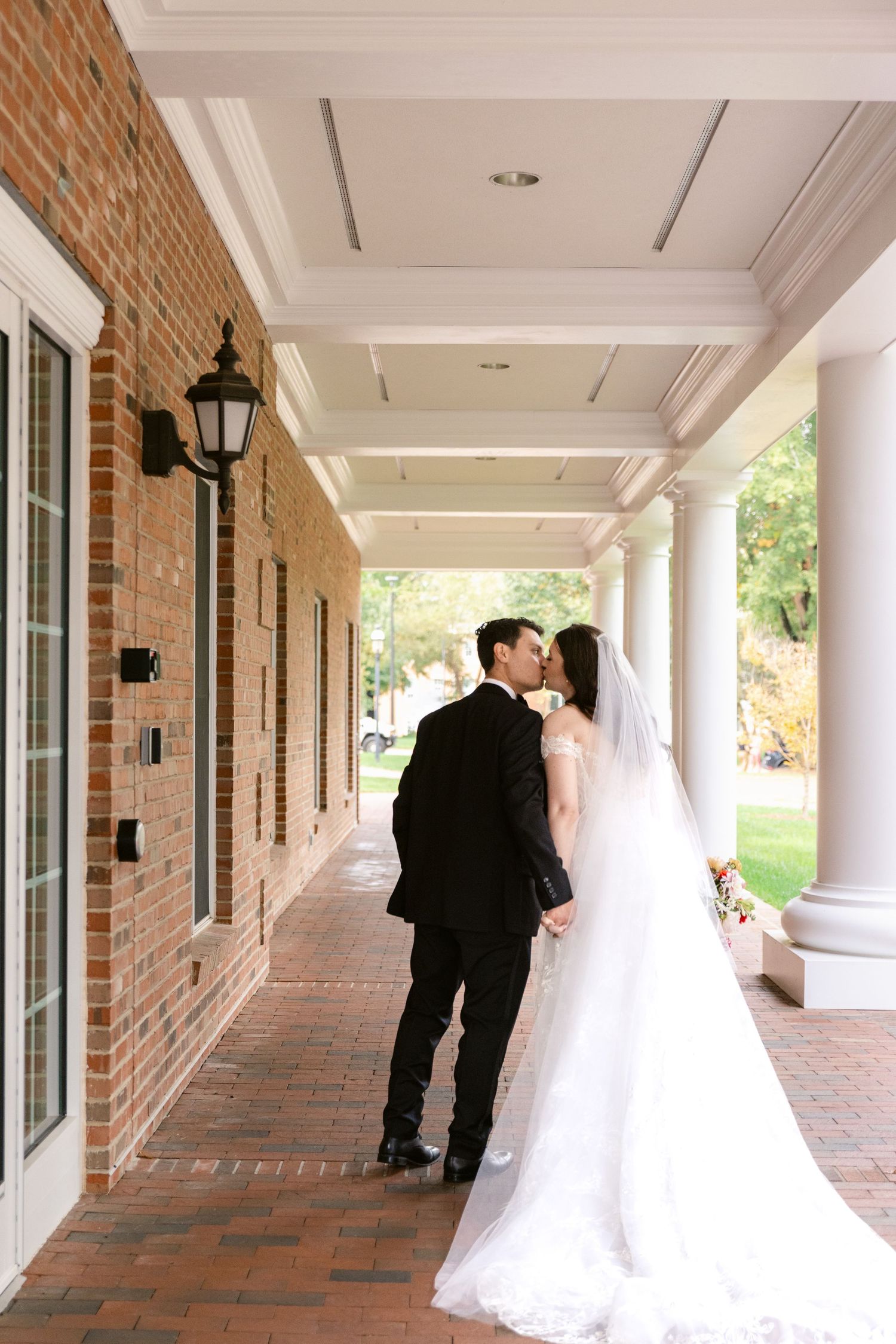 A sequence of romantic wedding photos showing a couple in formal attire walking along a brick columned hallway.