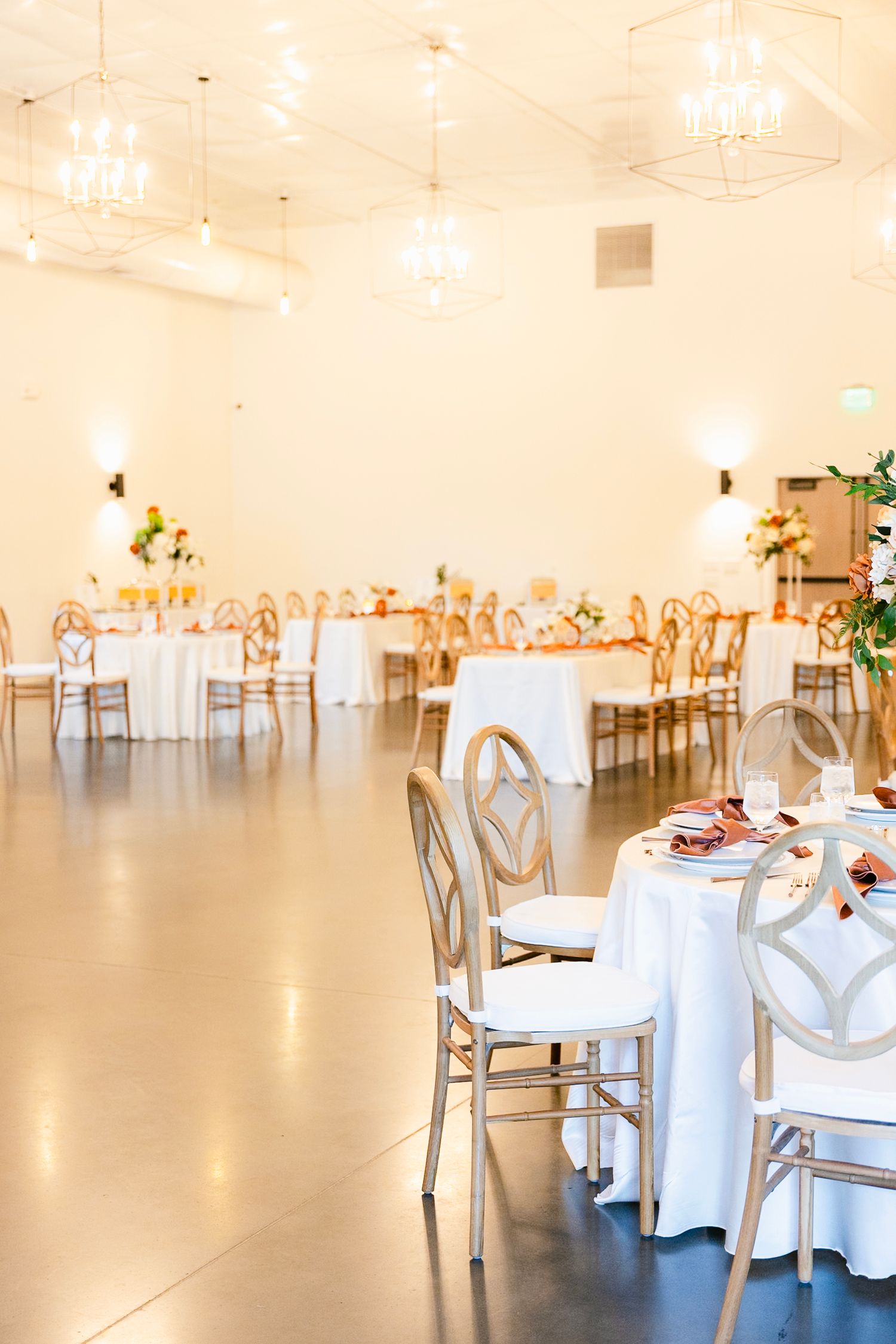 Elegant white wedding reception venue with round tables and modern chairs in a bright, minimalist space.