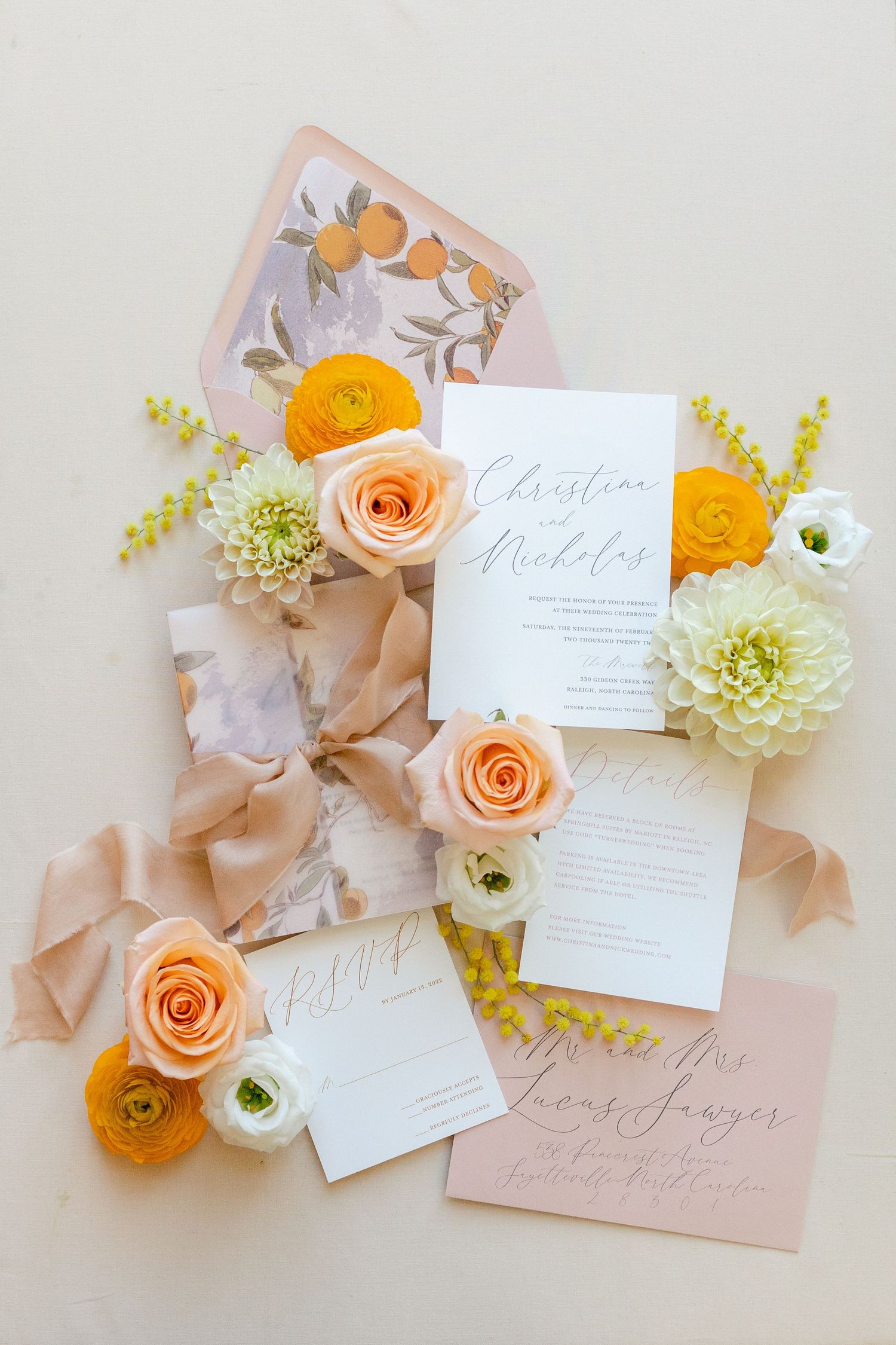 Wedding invitation suite with peach roses and orange ranunculus flowers on light pink paper.