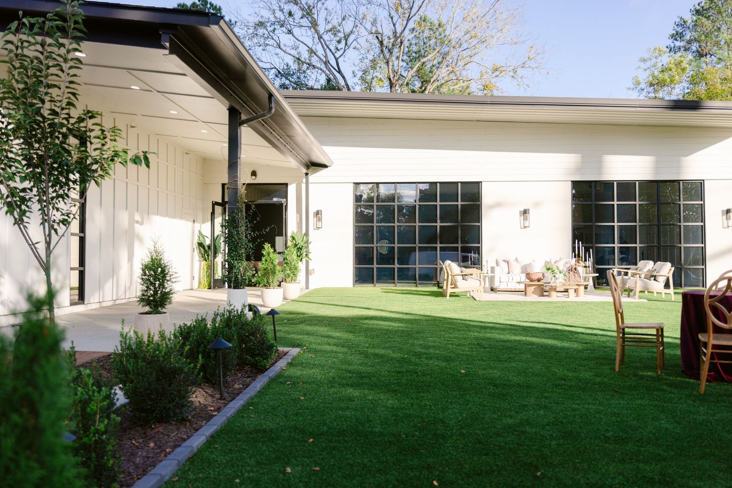 A panoramic view of a modern white house exterior with large windows and a well-maintained green lawn.
